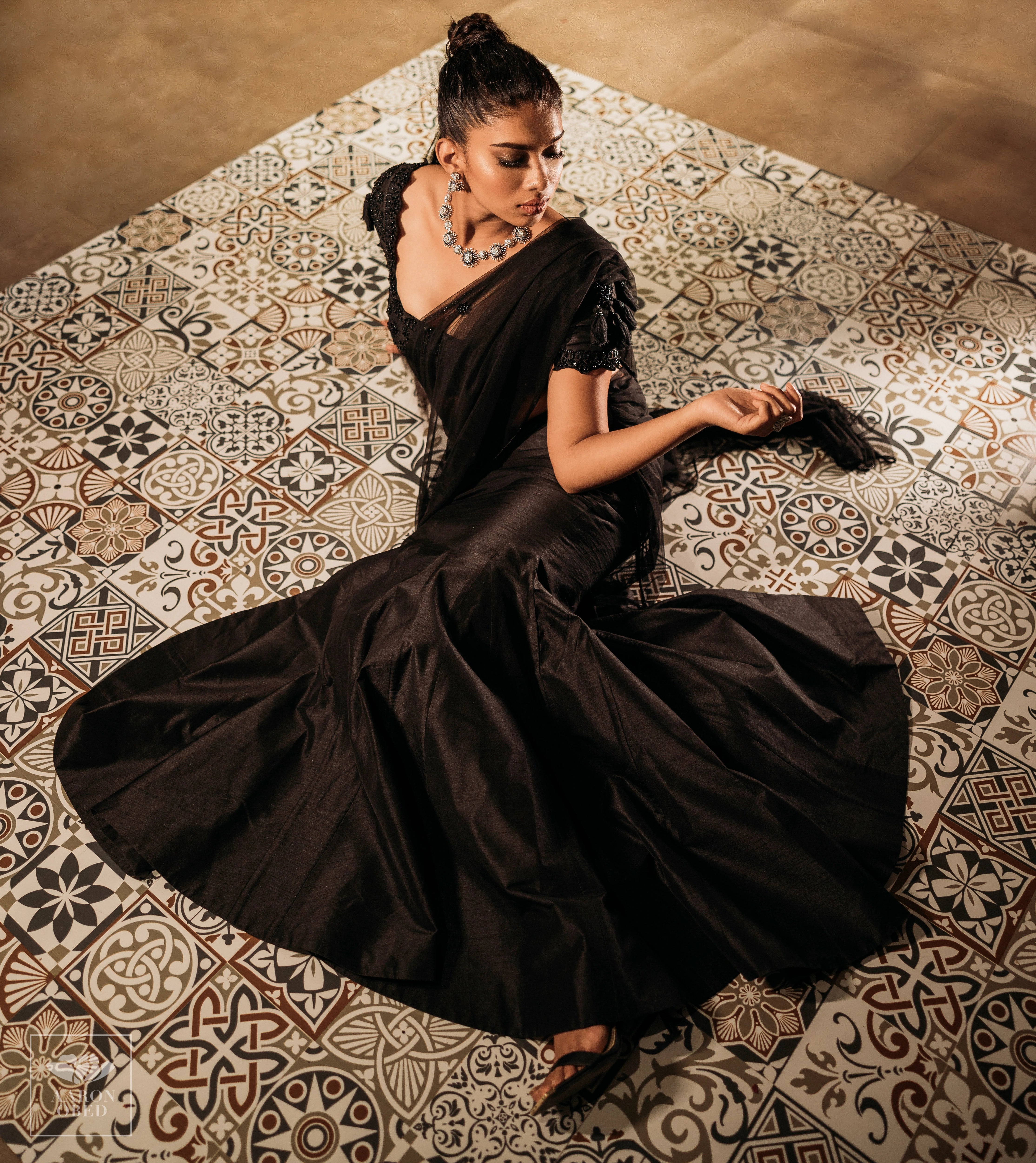 Actress Dushara Vijayan on the floor in a black tulle and raw silk draped mermaid lehenga, intricately handcrafted with beads, sequins and resham by team Archana Karthick.