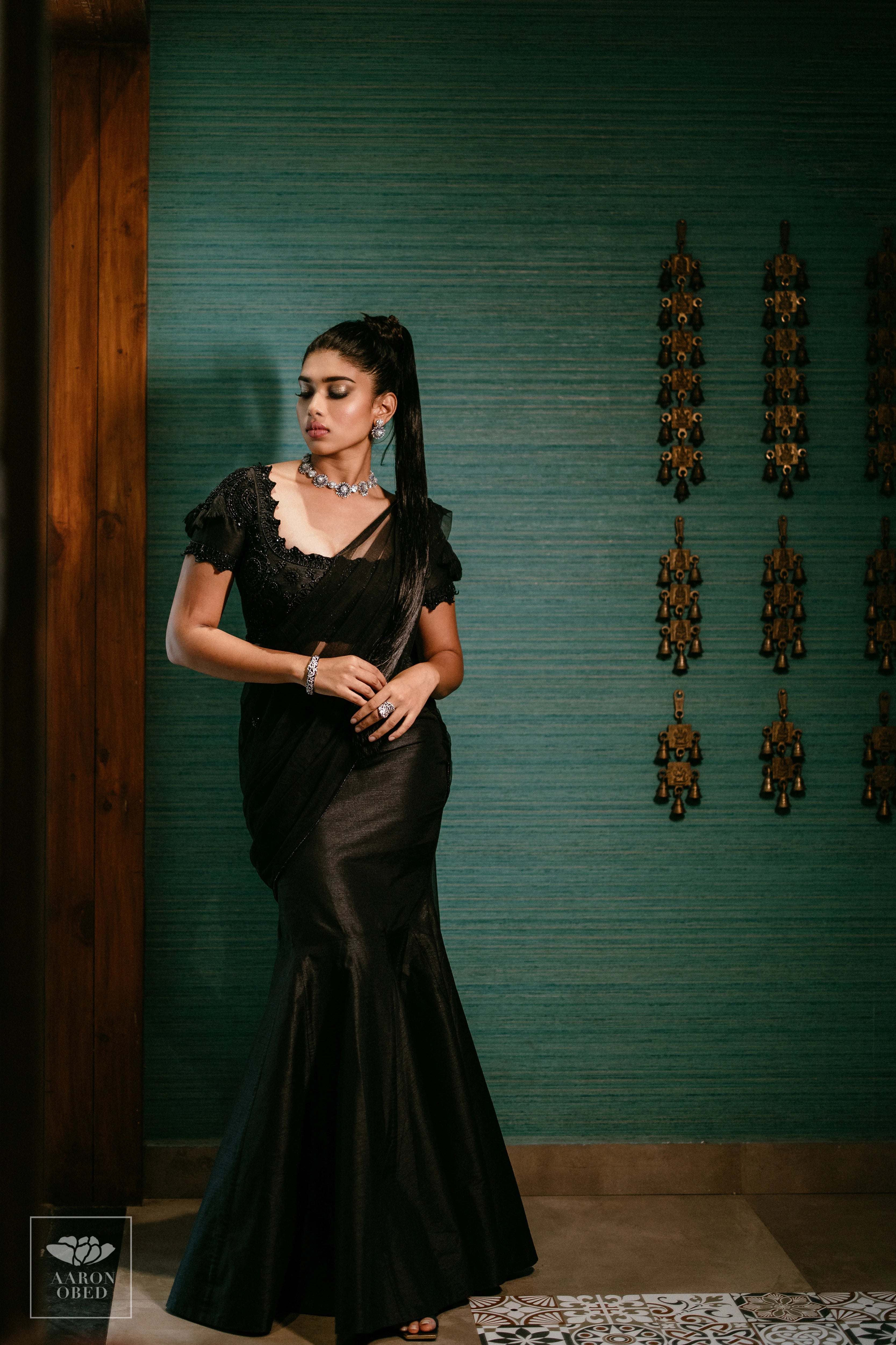 Actress Dushara Vijayan posing in a black tulle and raw silk draped mermaid lehenga, intricately handcrafted with beads, sequins and resham by team Archana Karthick.