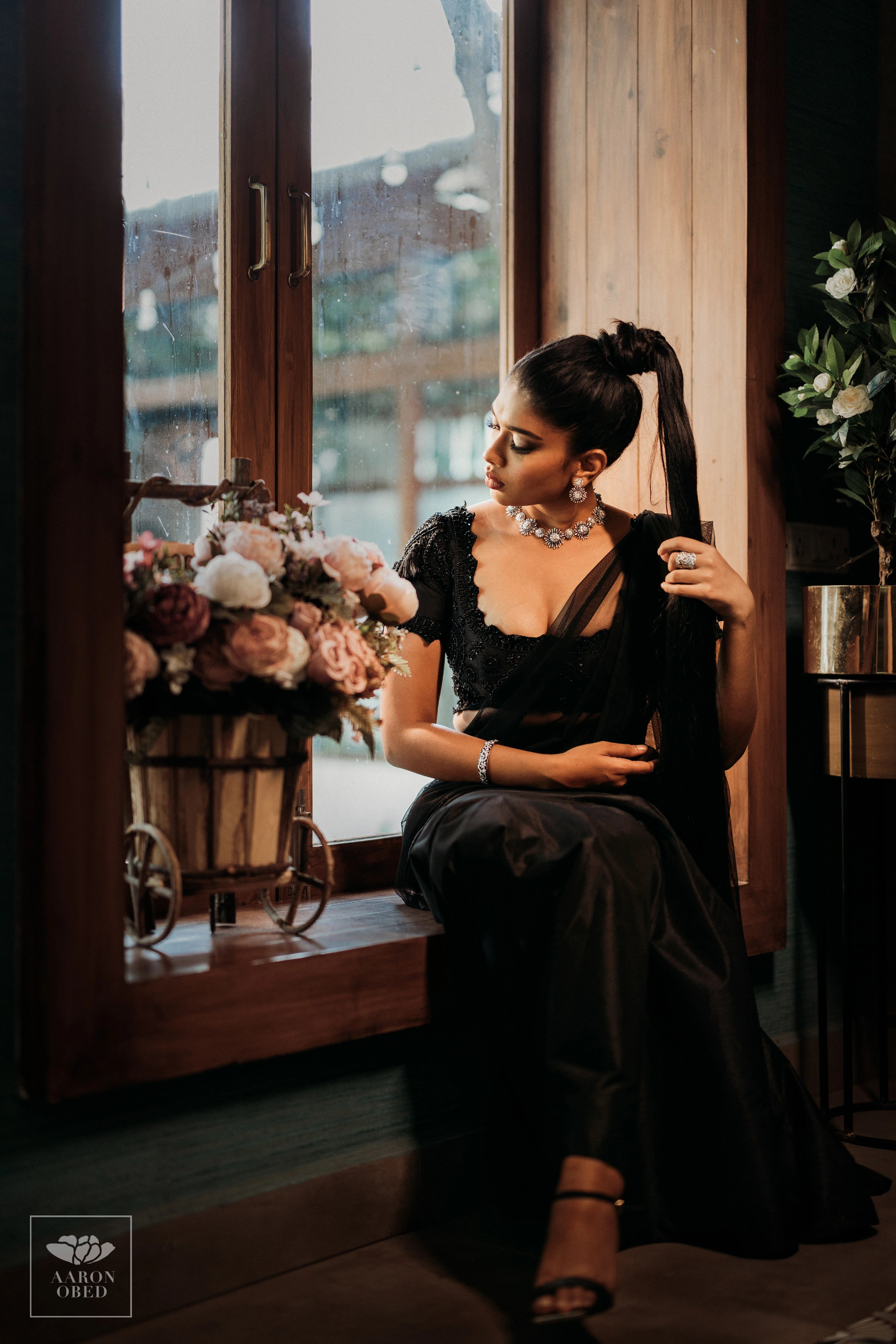 Actress Dushara Vijayan posing seated in a black tulle and raw silk draped mermaid lehenga, intricately handcrafted with beads, sequins and resham by team Archana Karthick.