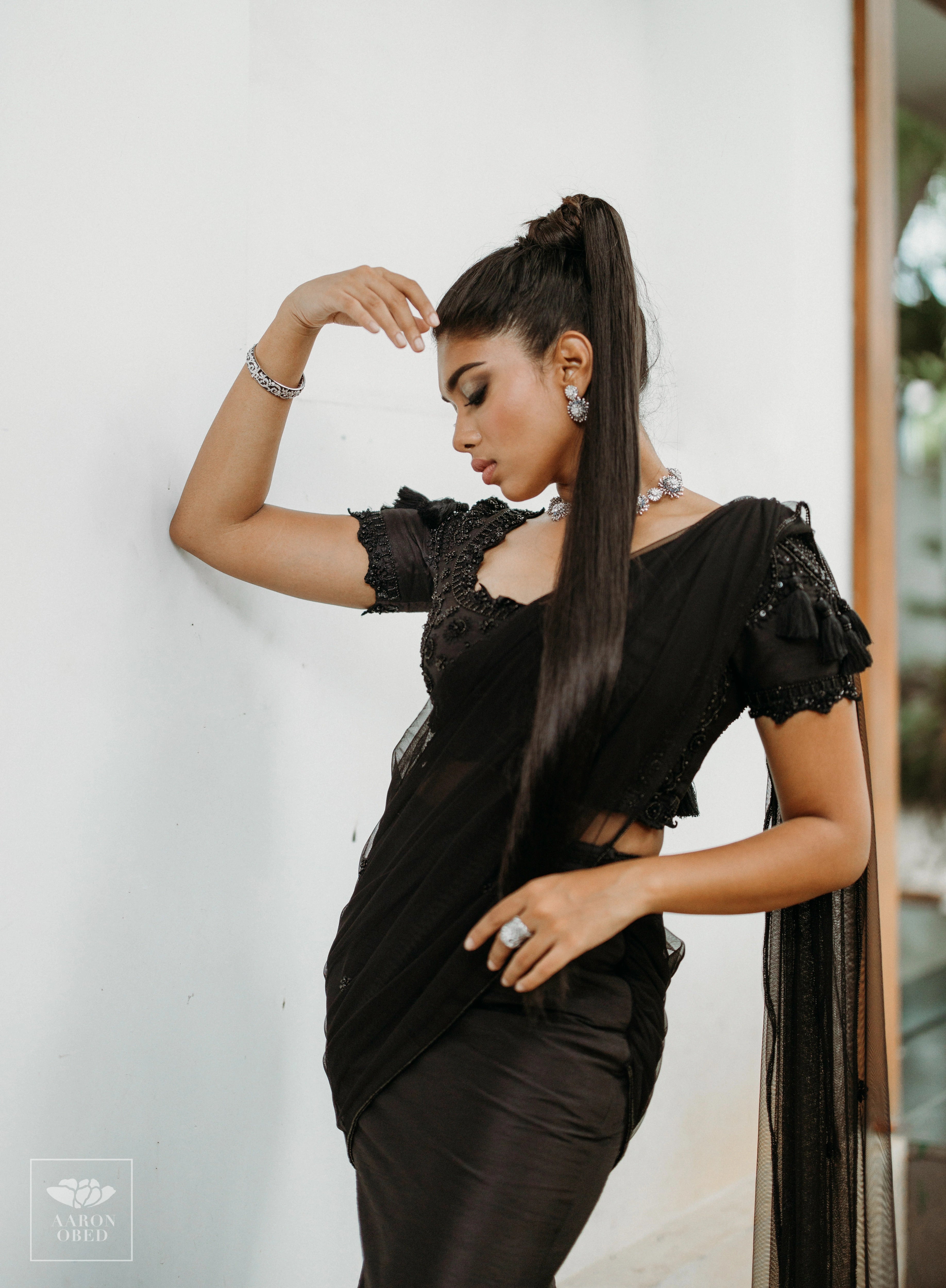 Actress Dushara Vijayan posing serious in a black tulle and raw silk draped mermaid lehenga, intricately handcrafted with beads, sequins and resham by team Archana Karthick.