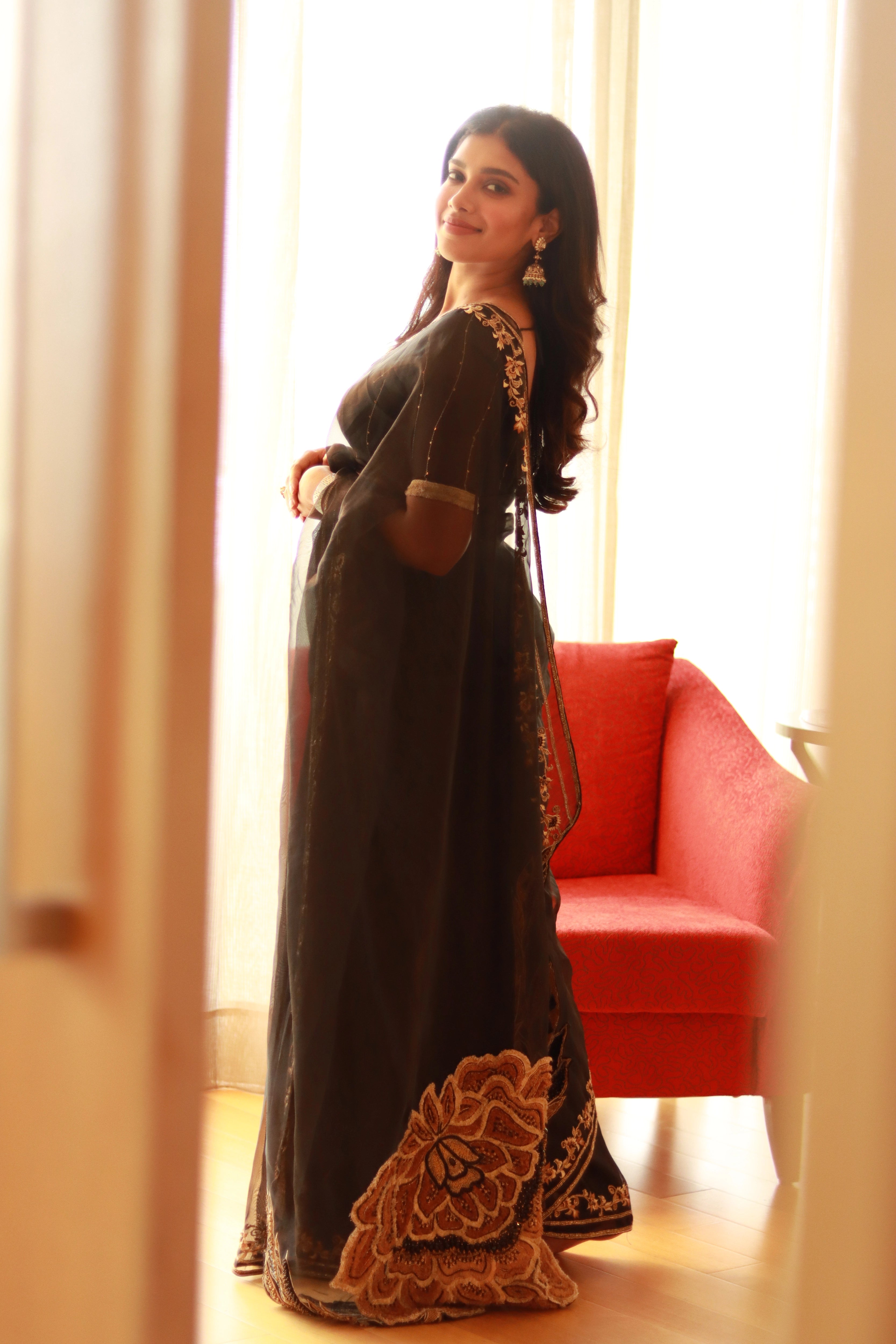 Actress Dushara Vijayan smiling in a black organza saree, intricately handcrafted with cutdana, zari, beads, sequins and resham by team Archana Karthick.