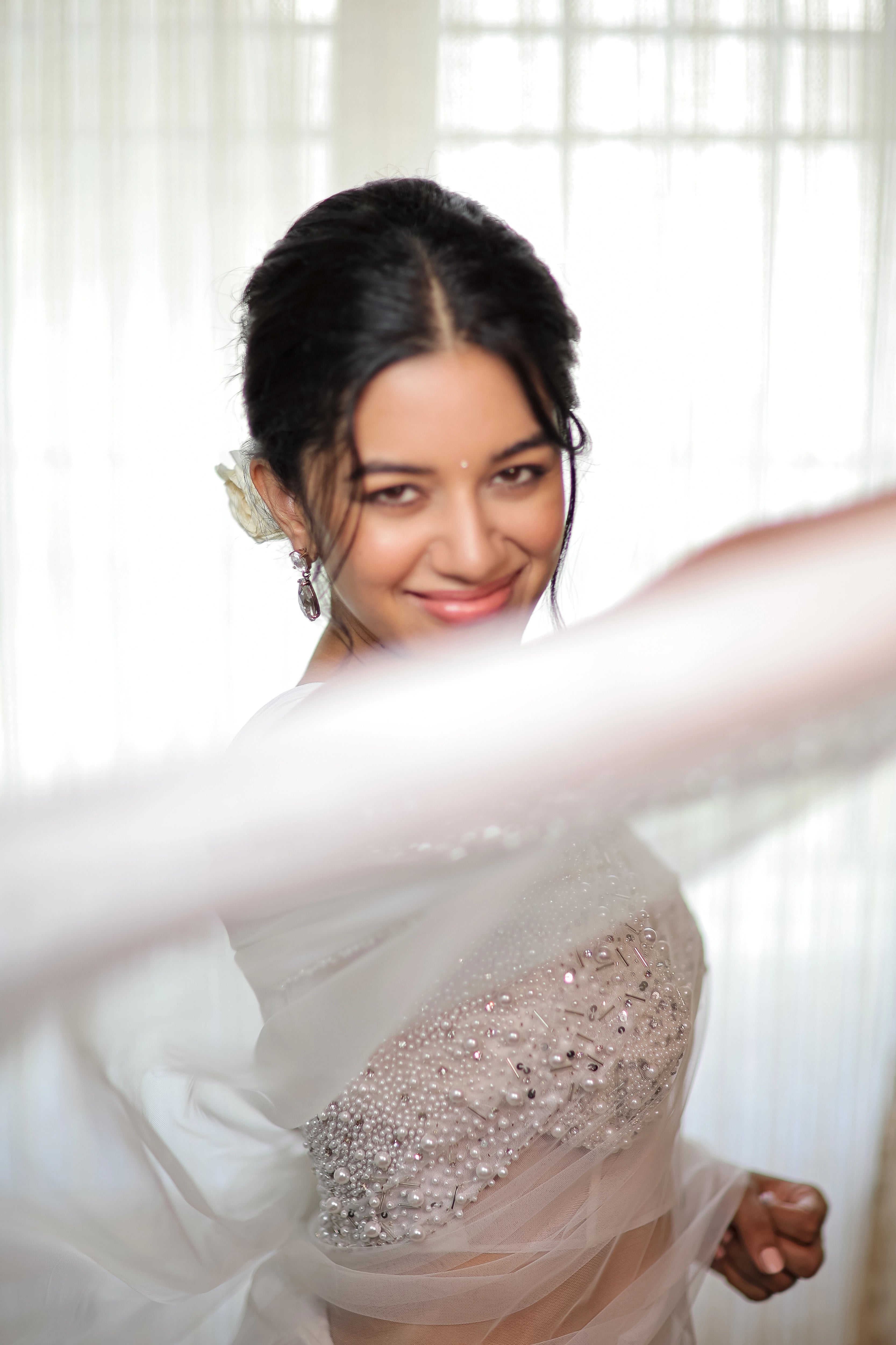 Actress Mirnalini Ravi posing for blouse side profile in a pearl white saree intricately embellished with pearls and cut beads, paired with an off-shoulder corset with cowl sleeves.