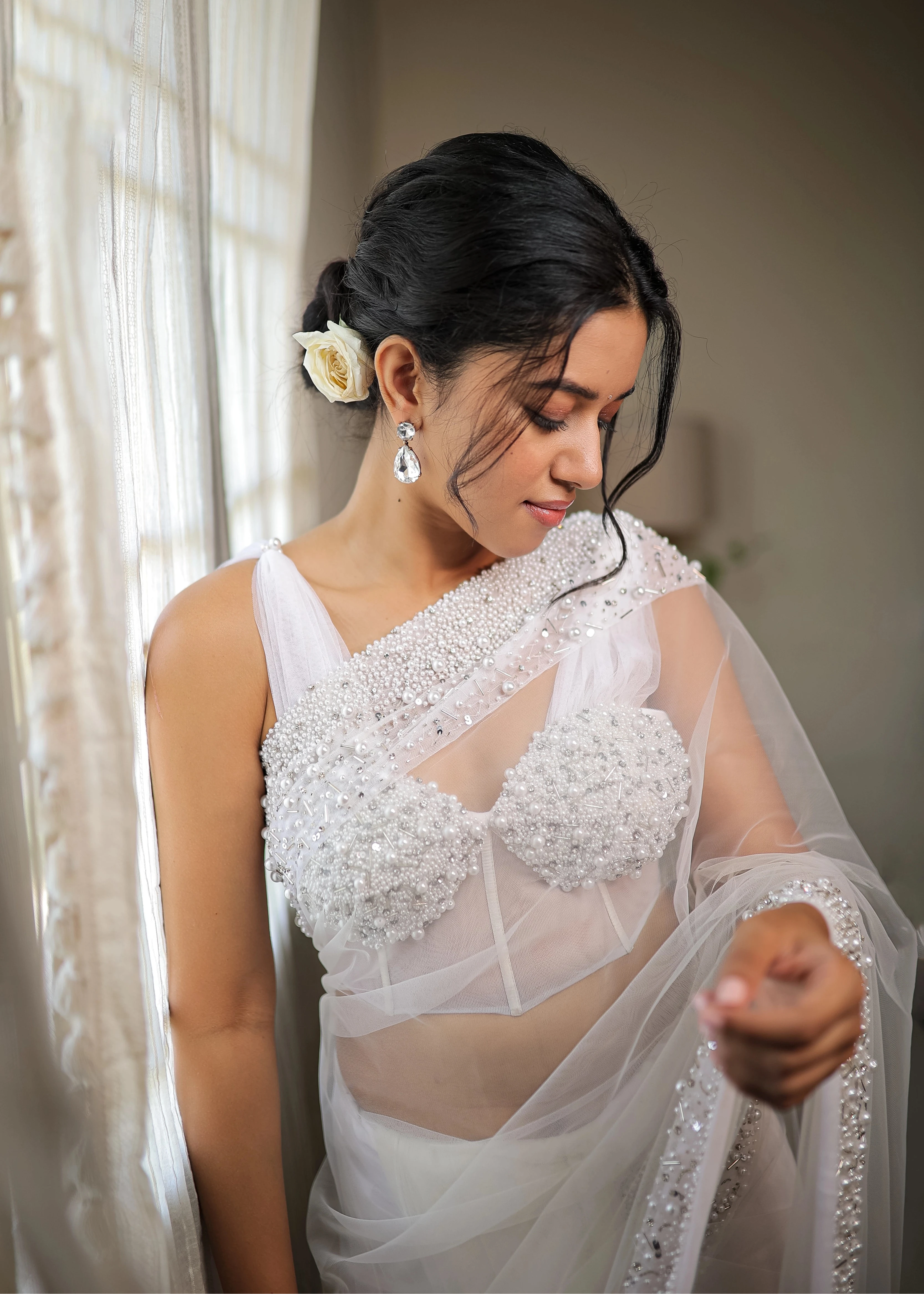 Actress Mirnalini Ravi posing for front profile in a pearl white saree intricately embellished with pearls and cut beads, paired with an off-shoulder corset with cowl sleeves.