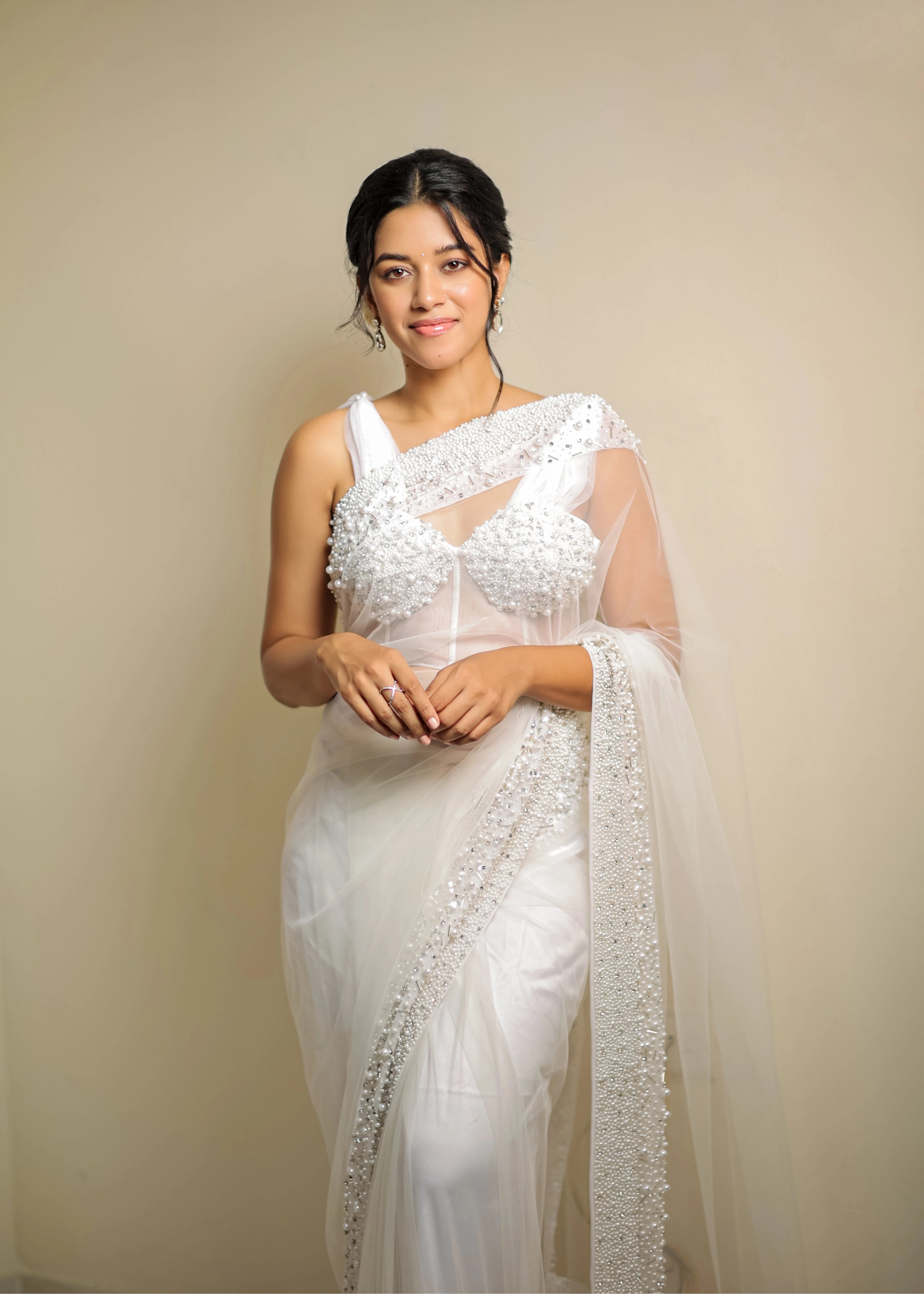 Actress Mirnalini Ravi posing in a pearl white saree intricately embellished with pearls and cut beads, paired with an off-shoulder corset with cowl sleeves.