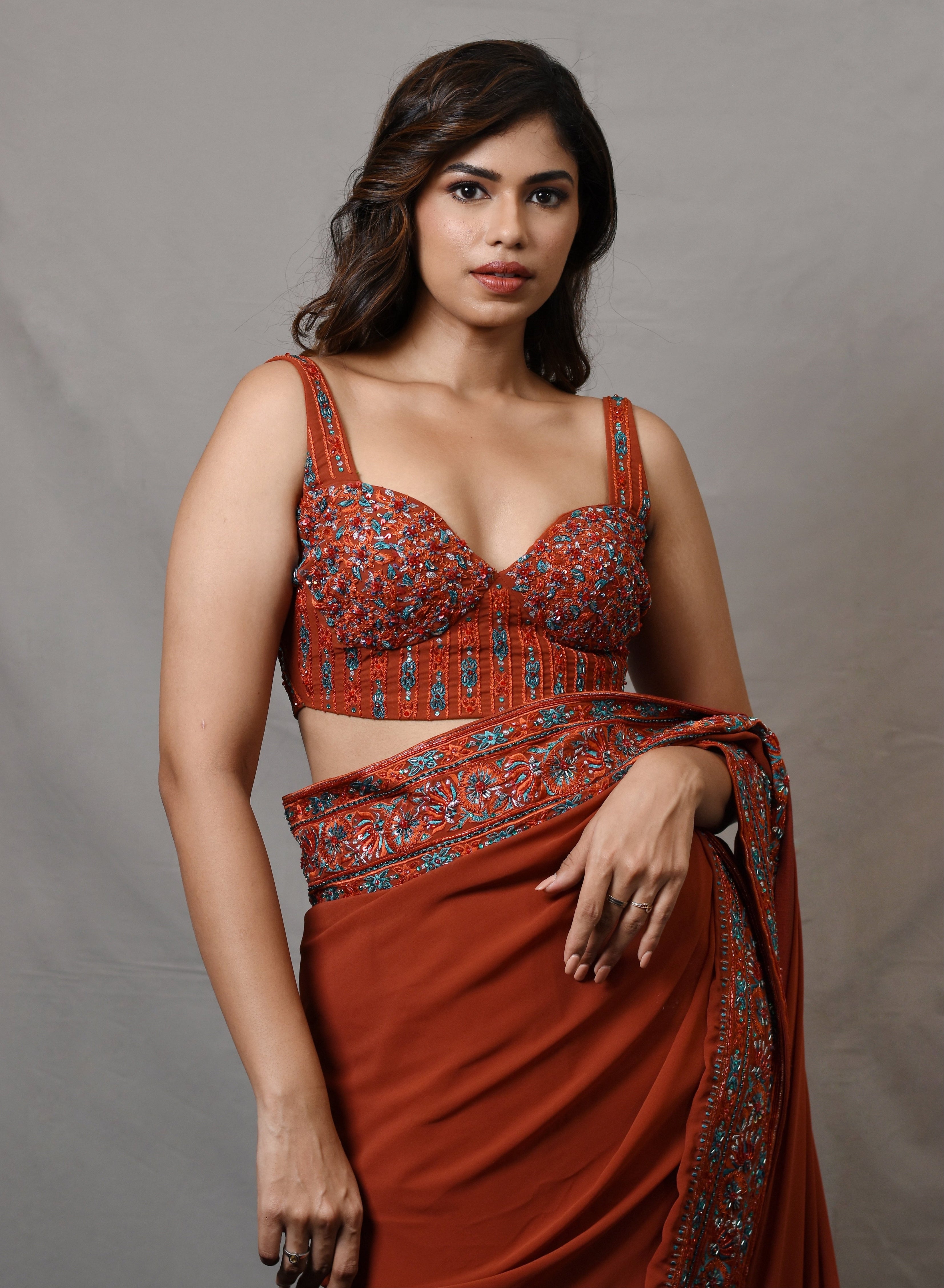 Actress Shrisha posing for corset detailings in a burnt orange crepe silk saree with an intricately handcrafted border and corset blouse from the Lo-Mance collection by Archana Karthick.
