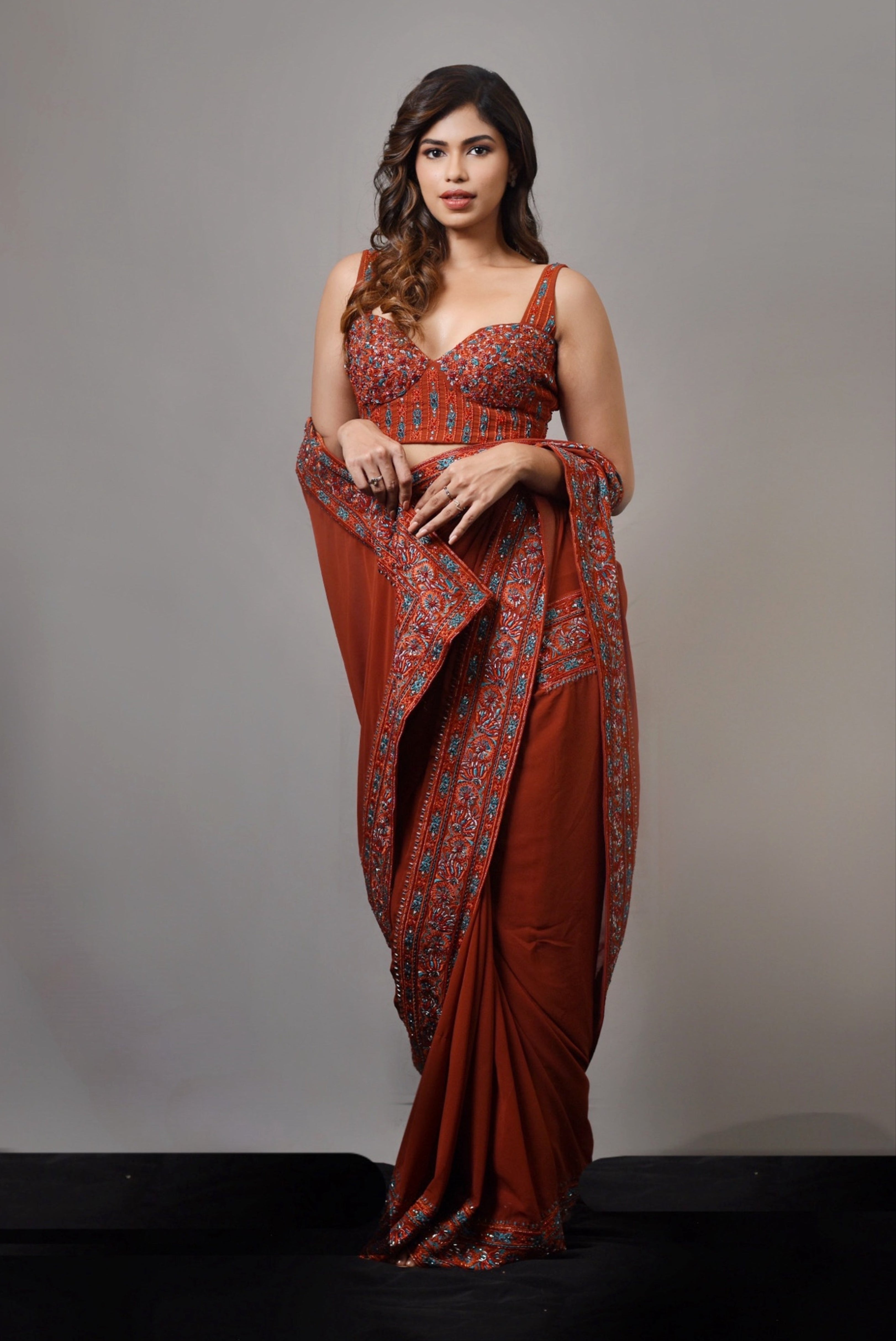 Actress Shrisha posing for full profile in a burnt orange crepe silk saree with an intricately handcrafted border and corset blouse from the Lo-Mance collection by Archana Karthick.