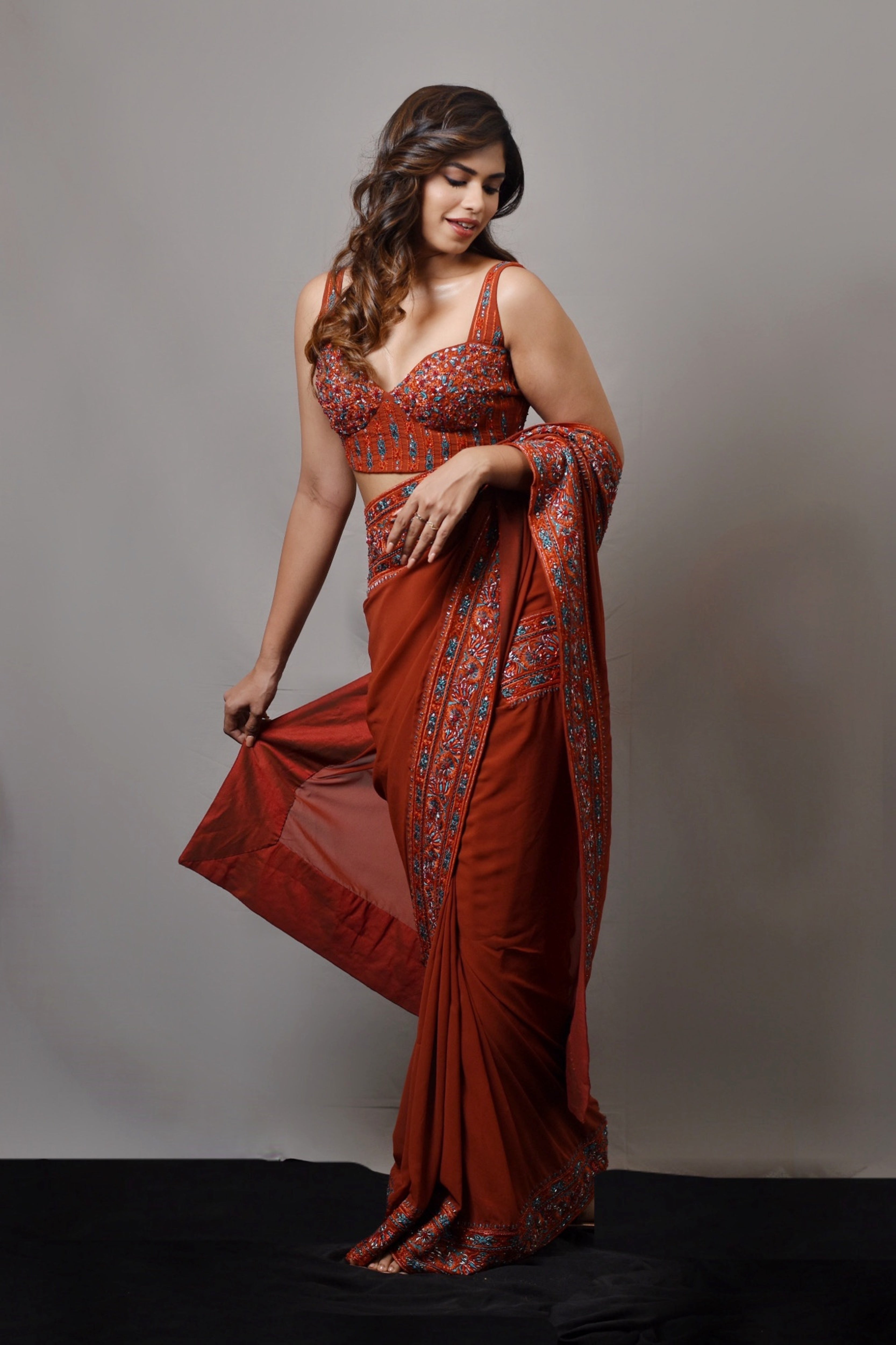 Actress Shrisha smiling in a burnt orange crepe silk saree with an intricately handcrafted border and corset blouse from the Lo-Mance collection by Archana Karthick.