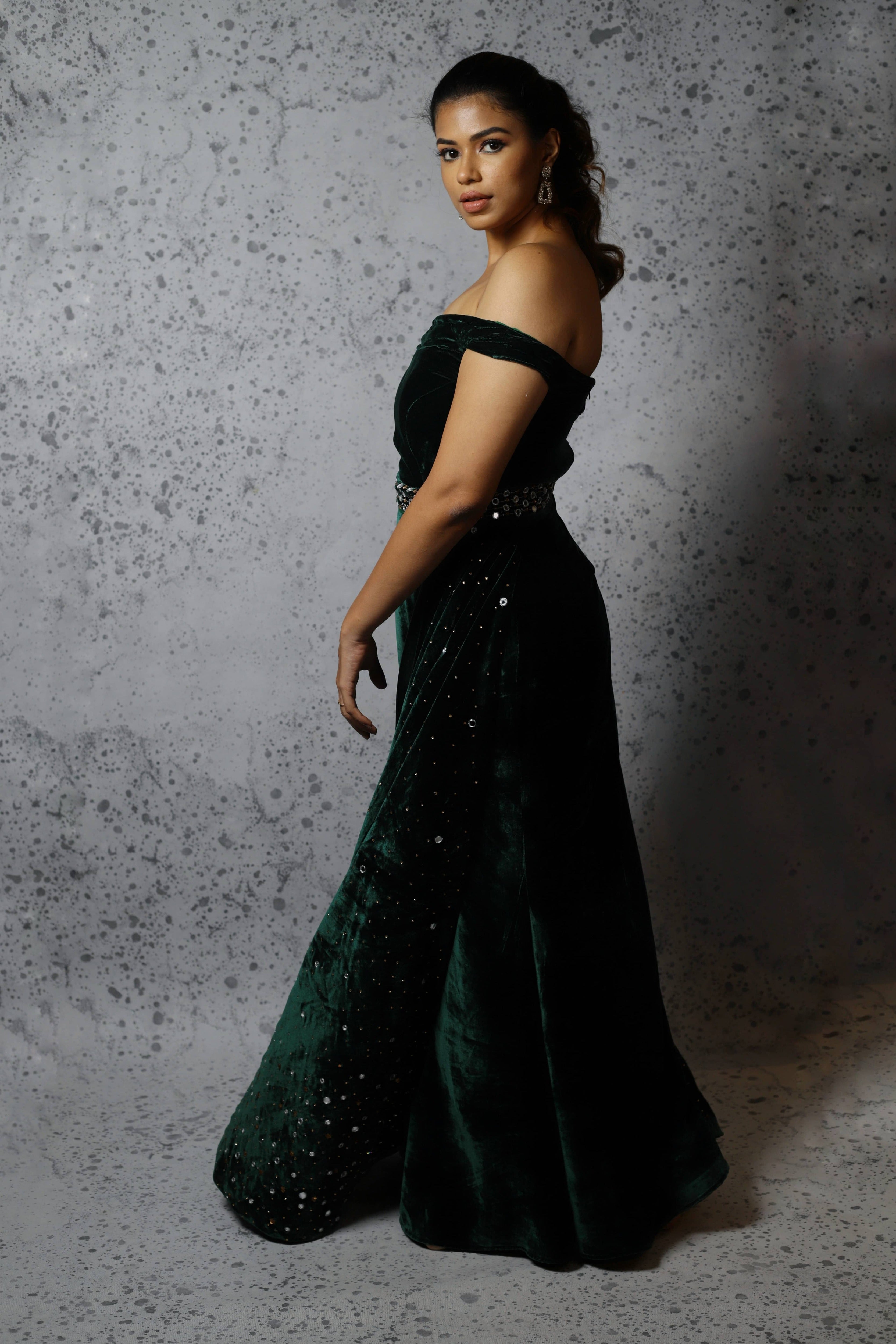 Actress Shrisha the niece of superstar actress Sridevi in a green velvet mermaid gown dress with detachable embellished belt and side trail. Side profile picture.