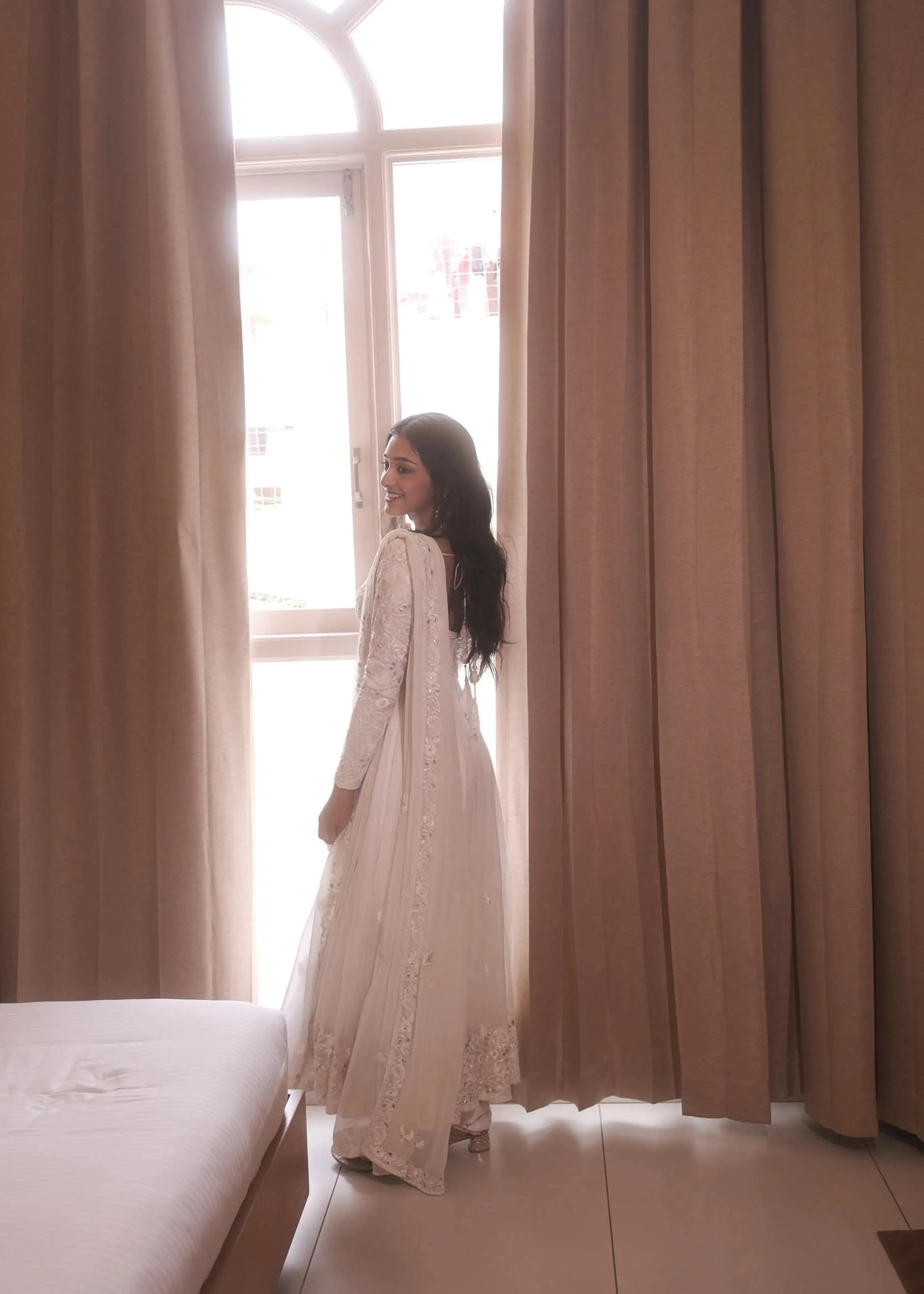 Actress & dancer Preity Mukhundhan smiling for photoshoot in a white georgette anarkali intricately handcrafted with gotapati, resham (chikanakri work) by team Archana Karthick.