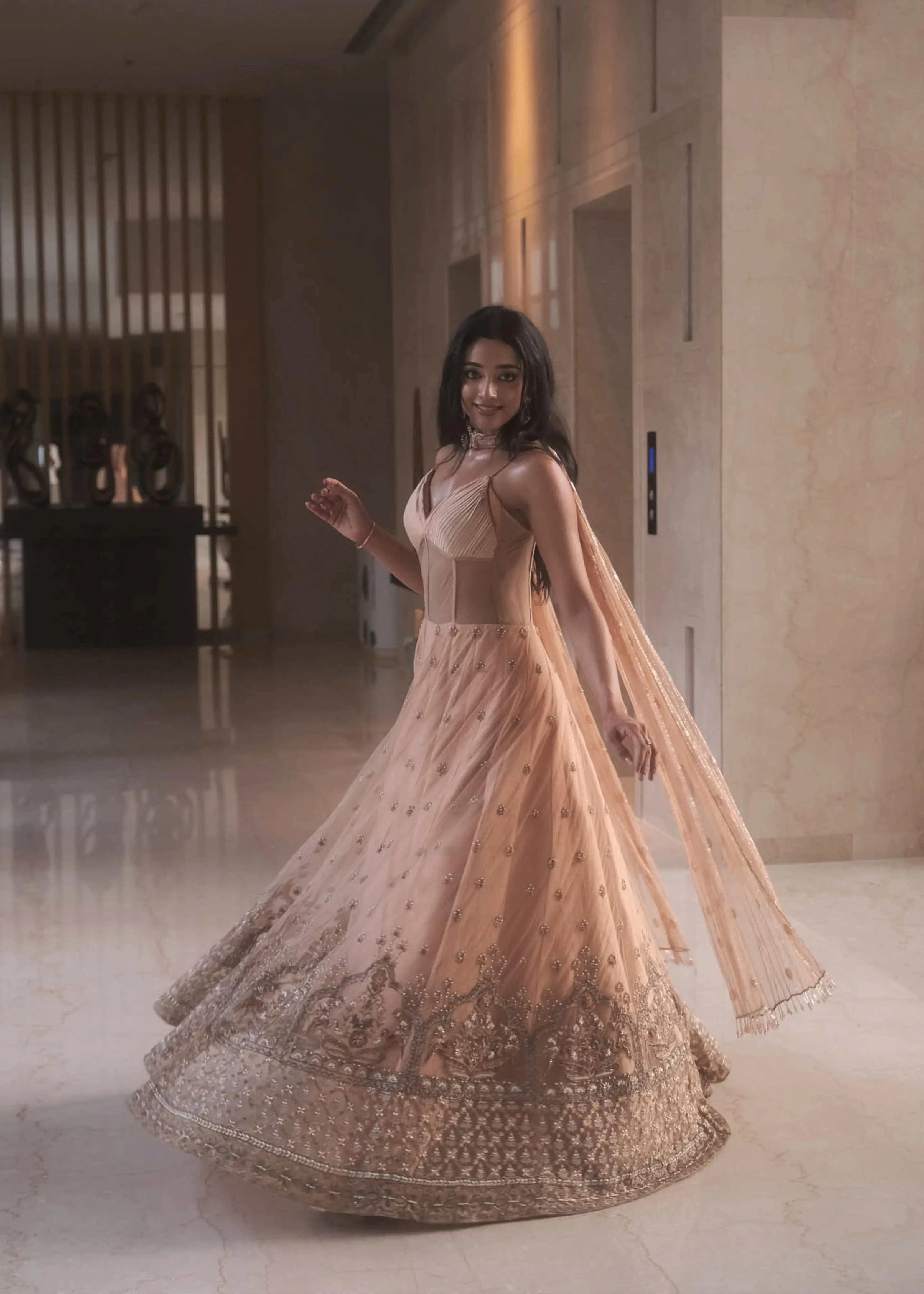 Actress & dancer Preity Mukhundhan twirling and smiling in a peach corset gown with draped dupatta attached at the neck, intricately handcrafted by team Archana Karthick.