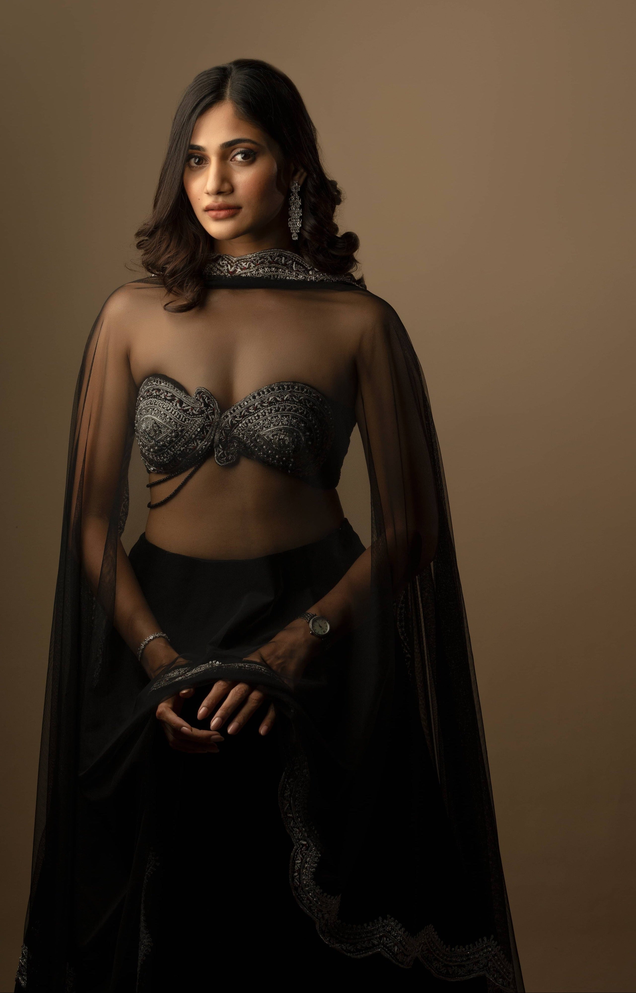 Bigg Boss fame and actress Losliya Mariyanesan in black velvet lehenga with silver embellishments on the borders and bralette. Posing here for full front profile with transparent dupatta showcasing the bralette