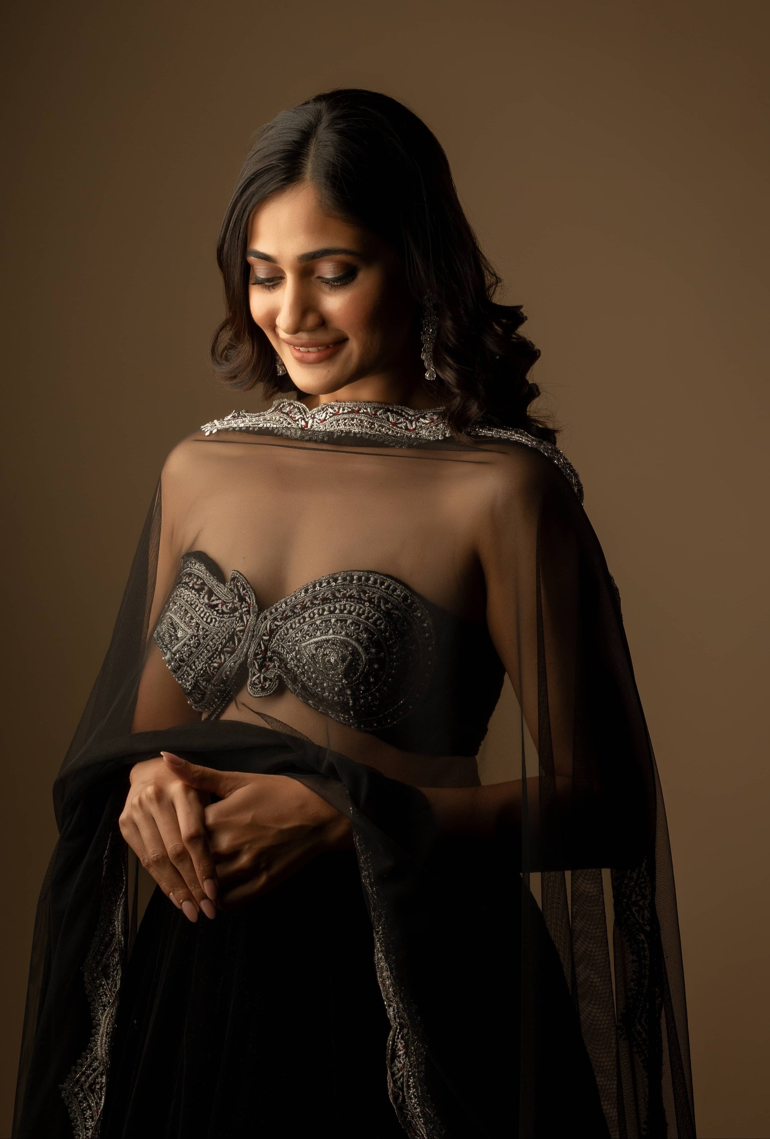 Bigg Boss fame and actress Losliya Mariyanesan in black velvet lehenga with silver embellishments on the borders and bralette. Posing looking down. bralette design is seen.