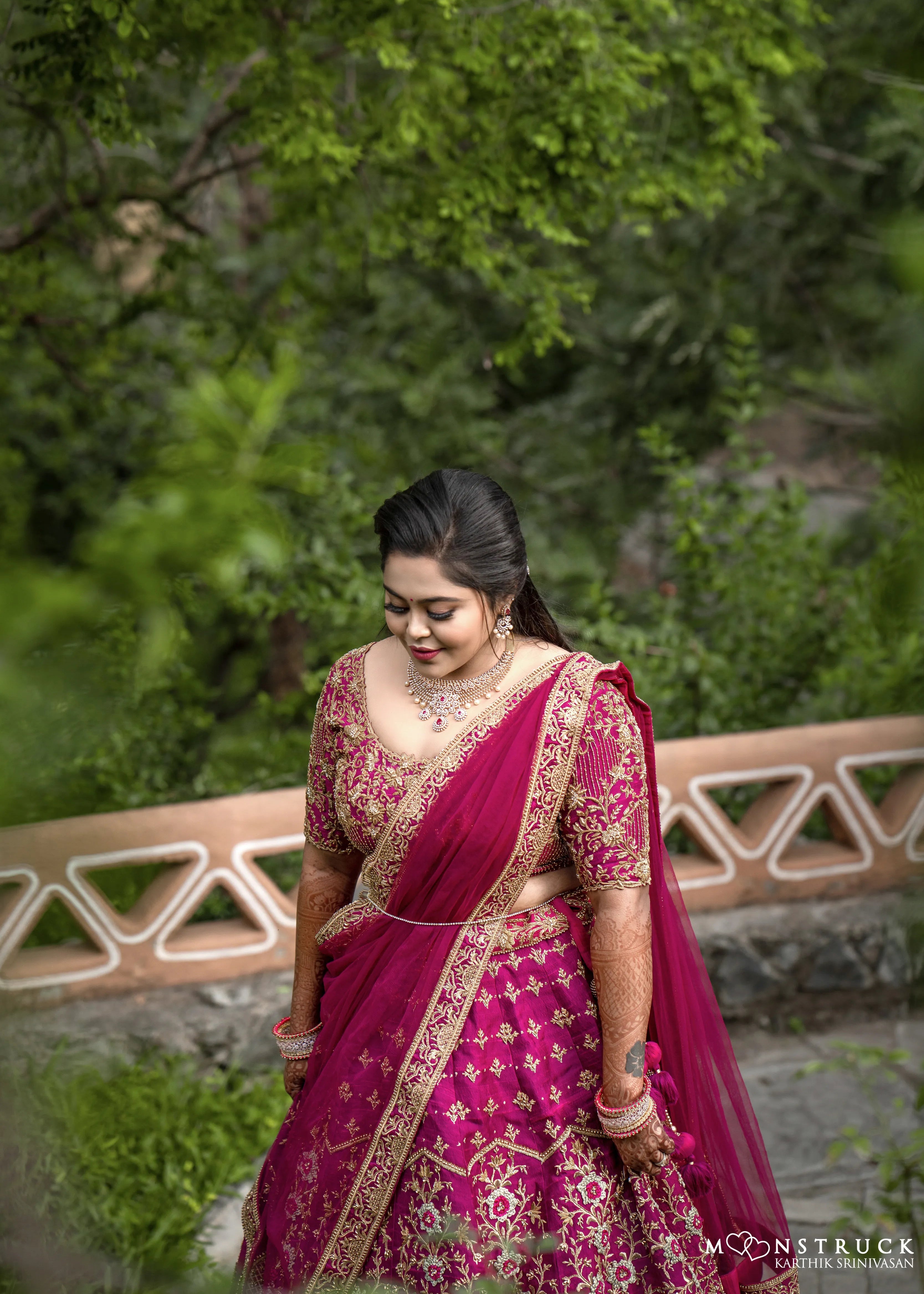 Bride Anjana from coimbatore looking down in a magenta red raw silk bridal lehenga designed by Archana Kartrhick.