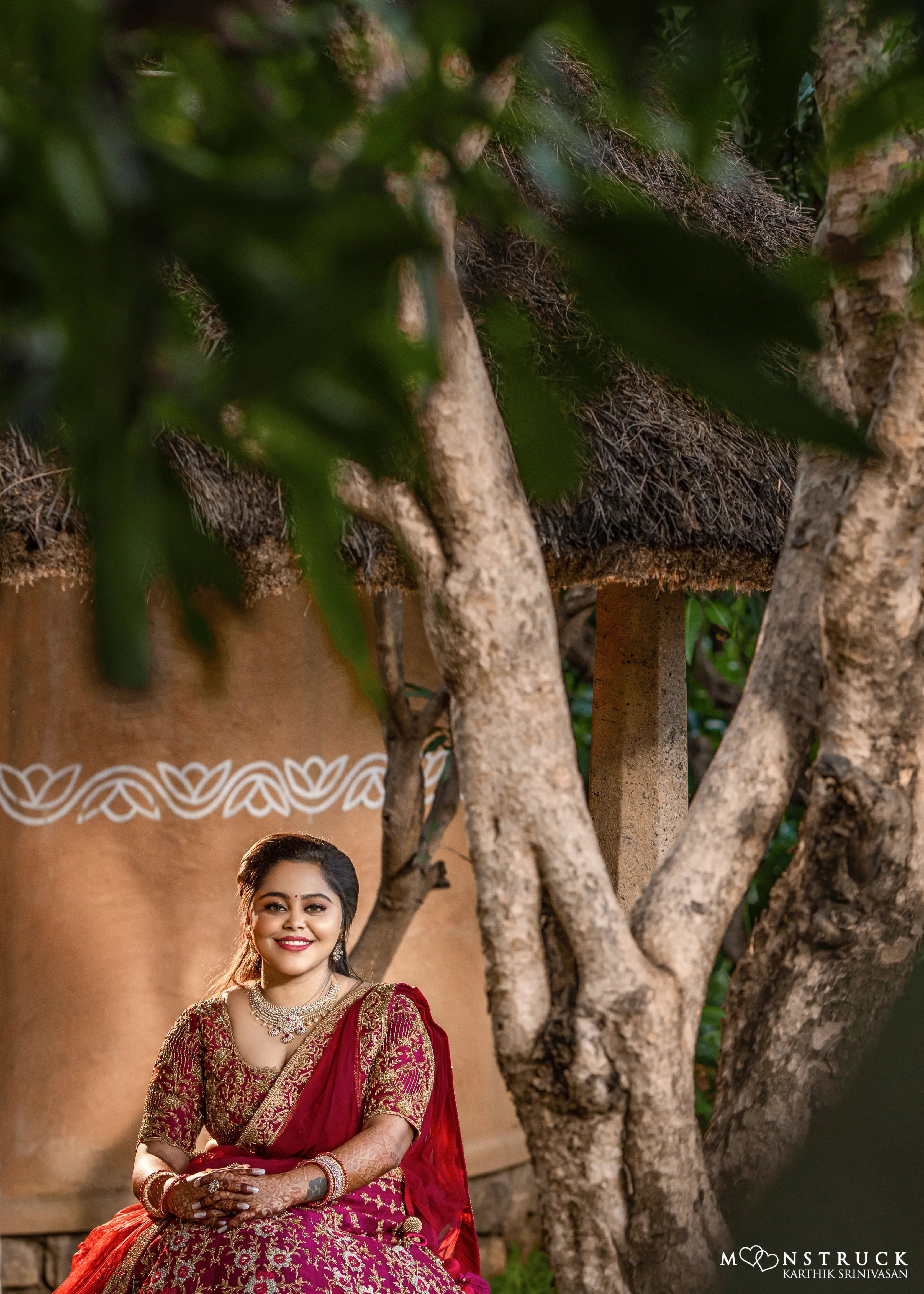 Bride Anjana from coimbatore posing seated in a magenta red raw silk bridal lehenga designed by Archana Kartrhick.