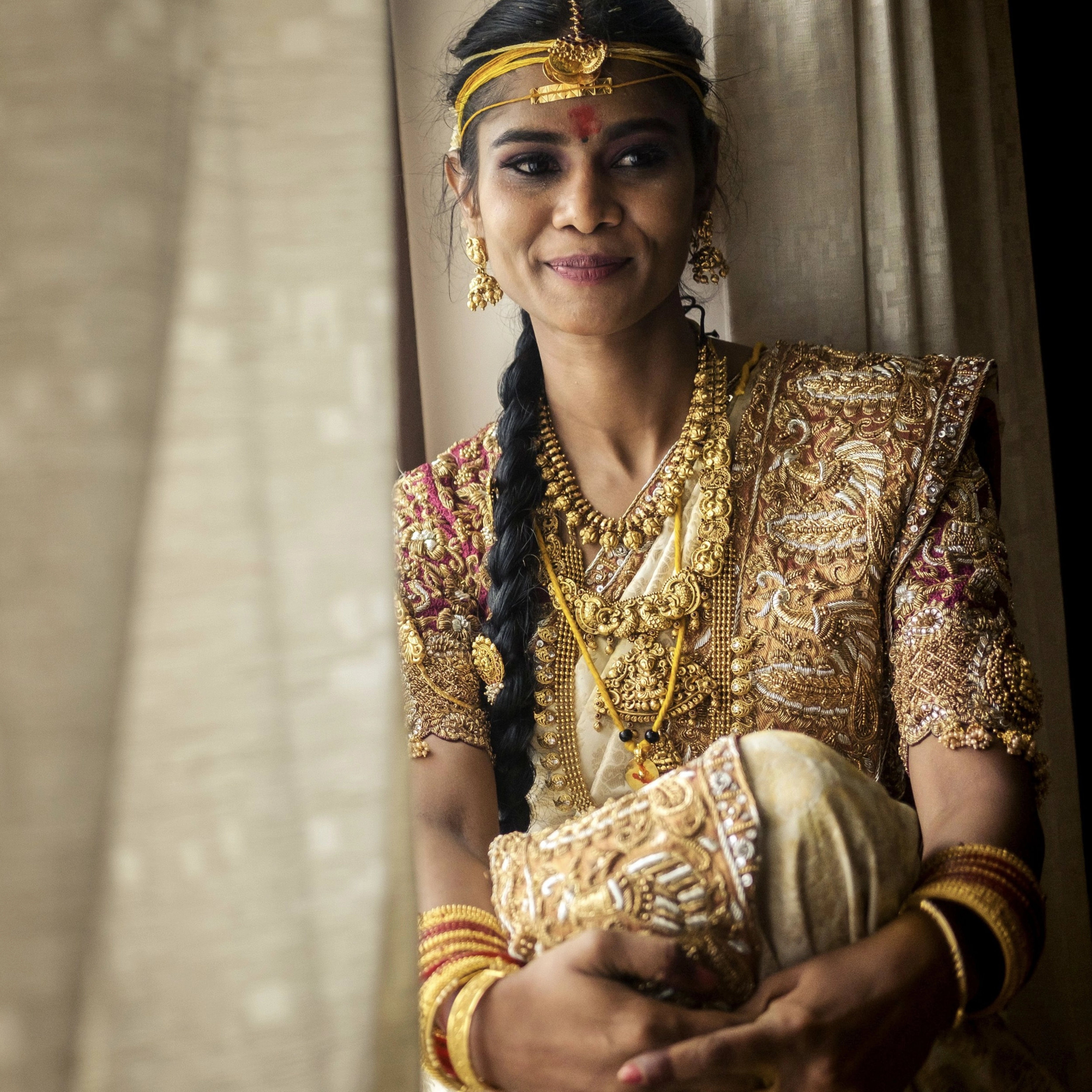 Bride Bhargavi smiling in a maroon palanquin concept silk blouse and saree border, intricately handcrafted with zardosi, beads, resham work, kundan and sequins by team Archana Karthick.