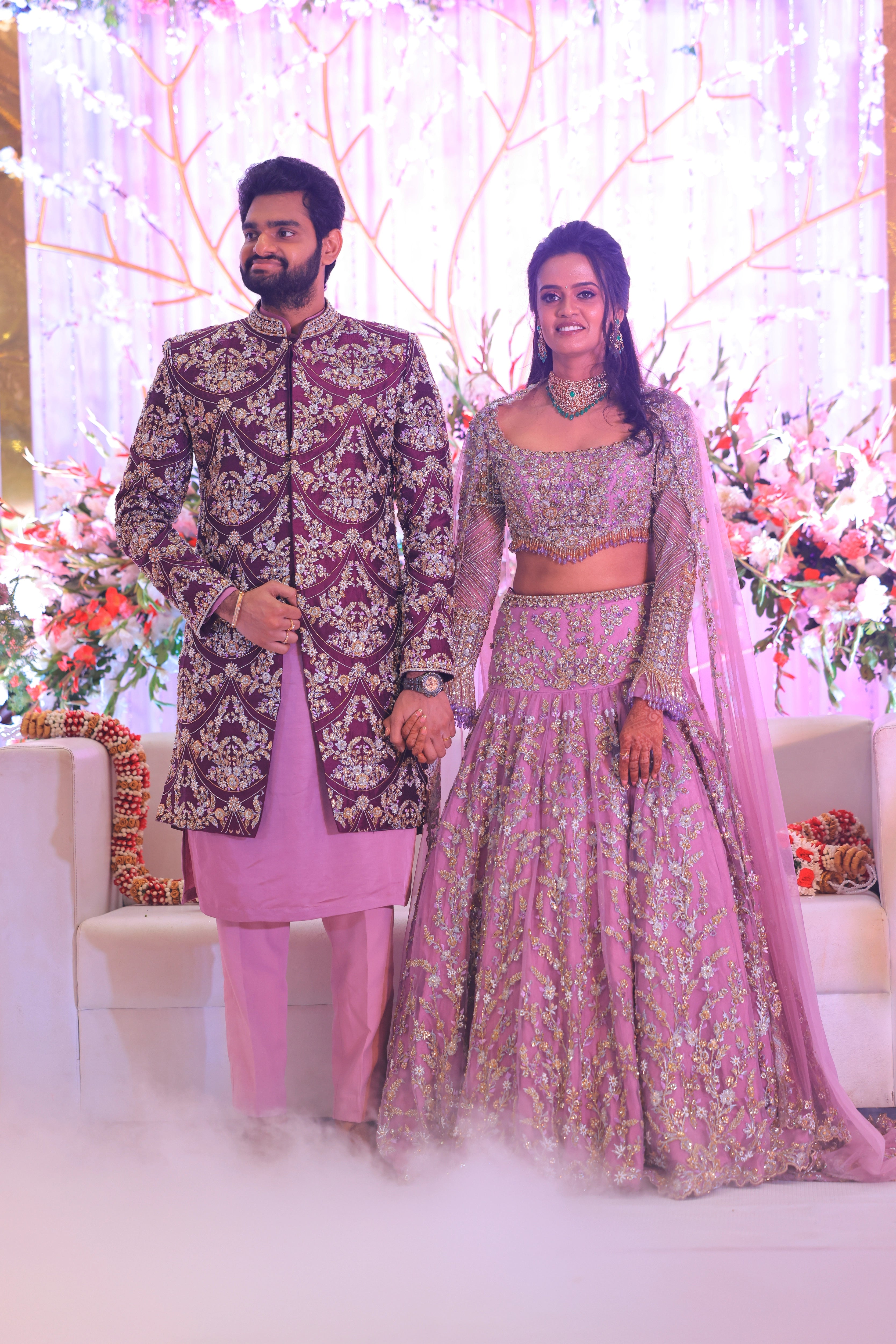 Bride Deepika holding hands with groom in lavender raw silk lehenga, intricately handcrafted with sequins, cutdana, beads, crystals, rhinestones and zardozi by team Archana Karthick.
