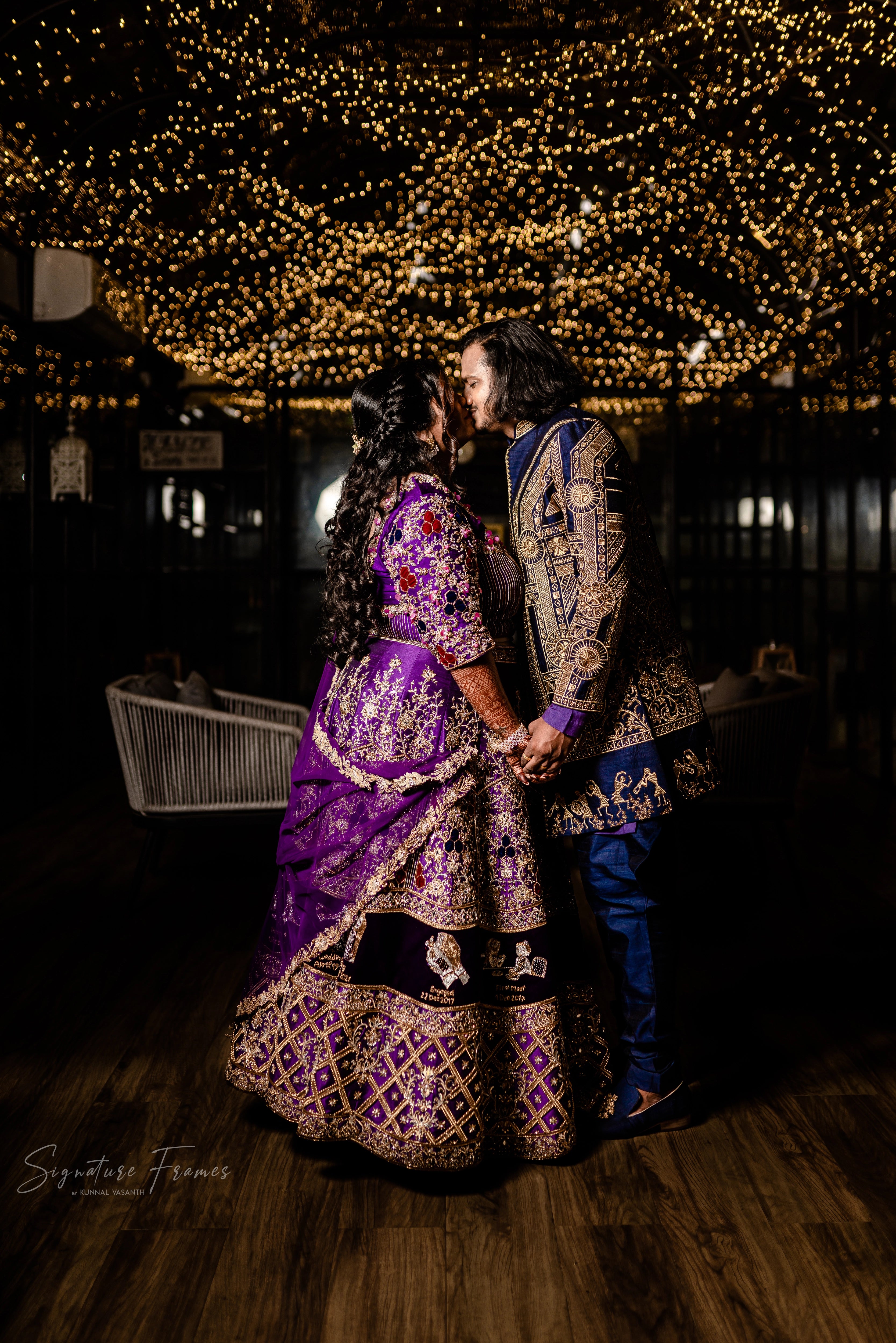 Bride & Groom posing in a purple raw silk lehenga and navy Indowestern outfit, handcrafted with mirrors, sequins, cutdana, beads and appliques by team Archana Karthick