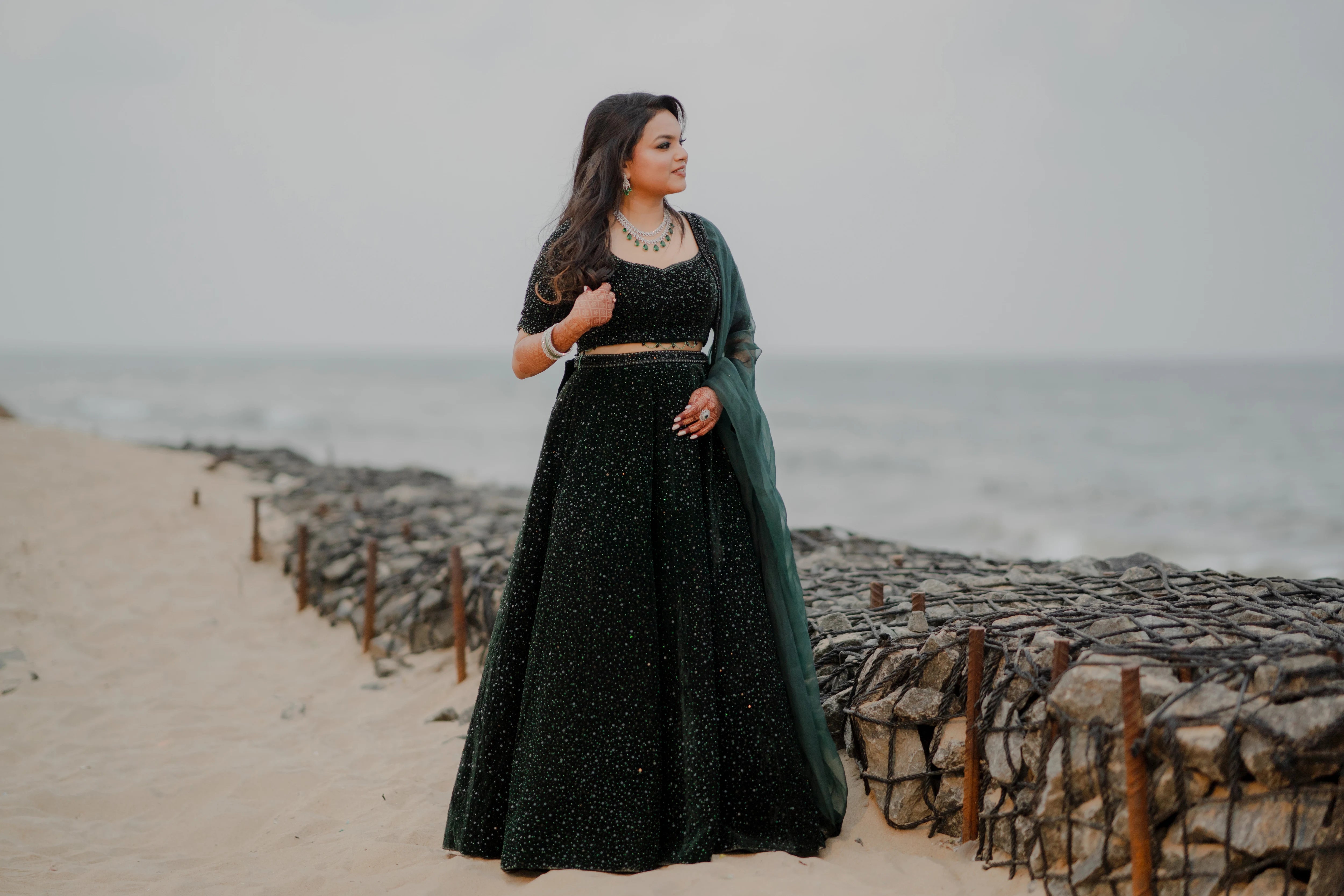 Bride Haripriya from USA posing on the beach in a bottle green velvet lehenga, intricately handcrafted with sequins, cutdana, beads and crystals by team Archana Karthick.
