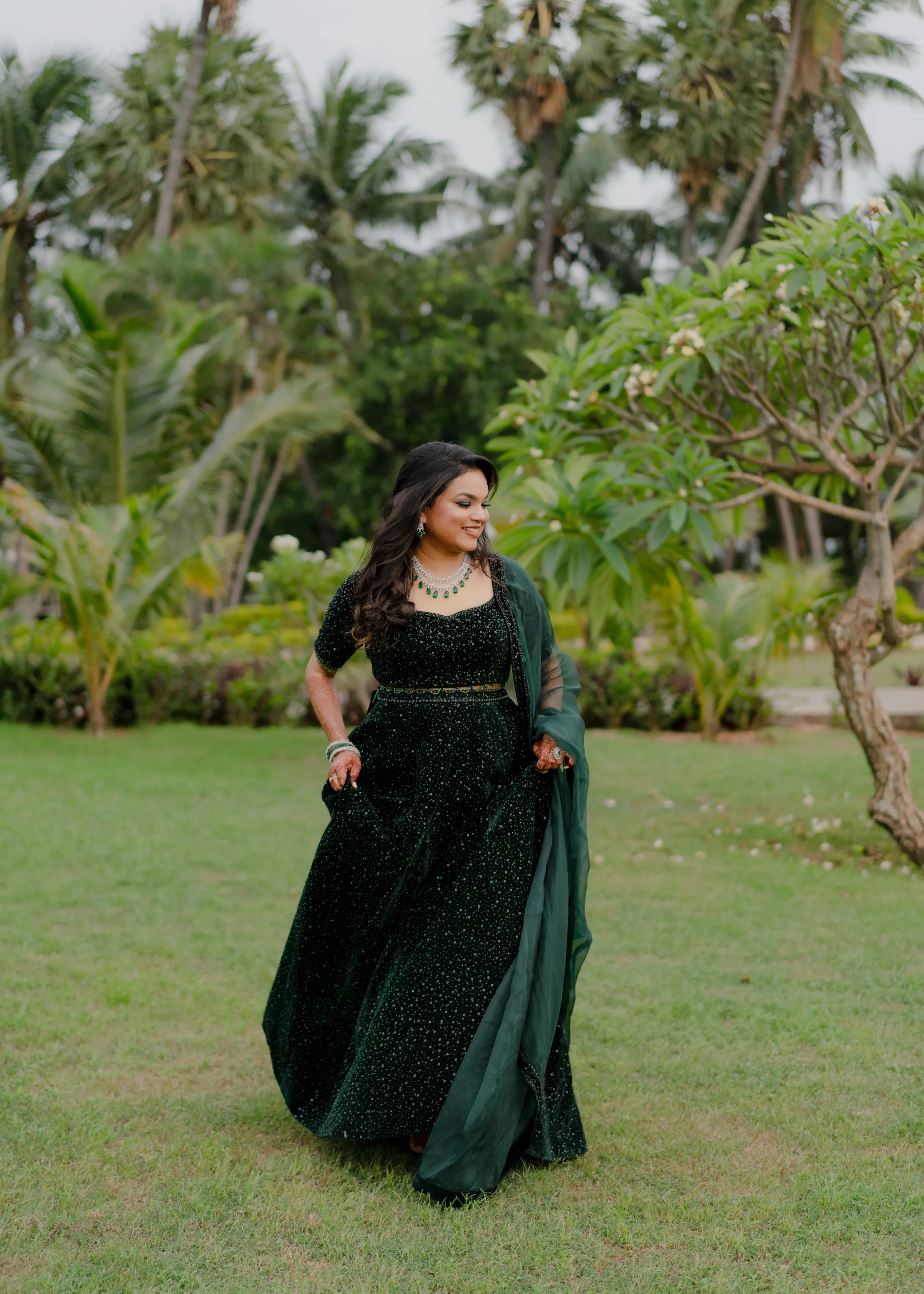 Bride Haripriya from USA posing on the lawn in a bottle green velvet lehenga, intricately handcrafted with sequins, cutdana, beads and crystals by team Archana Karthick.