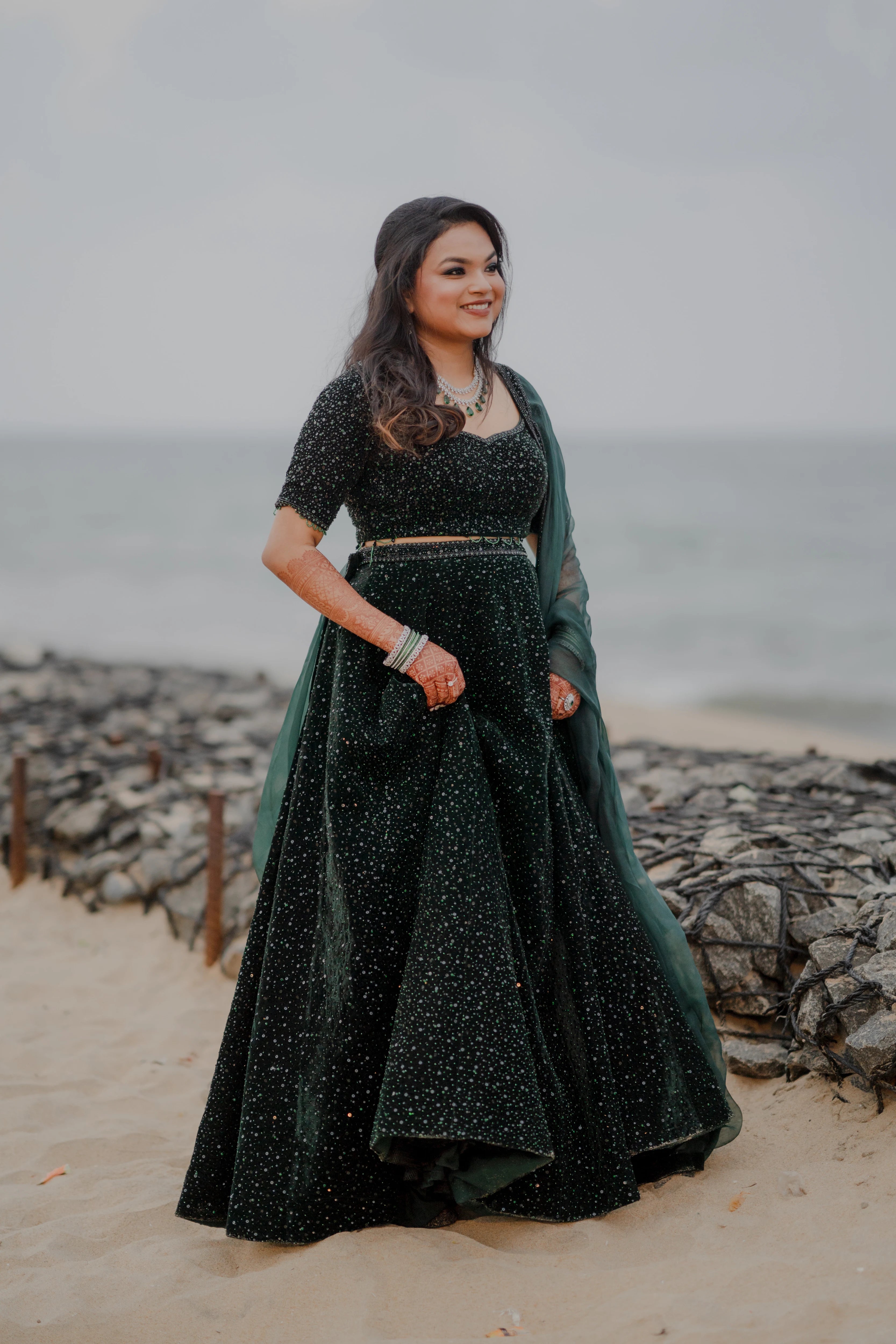 Bride Haripriya from USA smiling in a bottle green velvet lehenga, intricately handcrafted with sequins, cutdana, beads and crystals by team Archana Karthick.