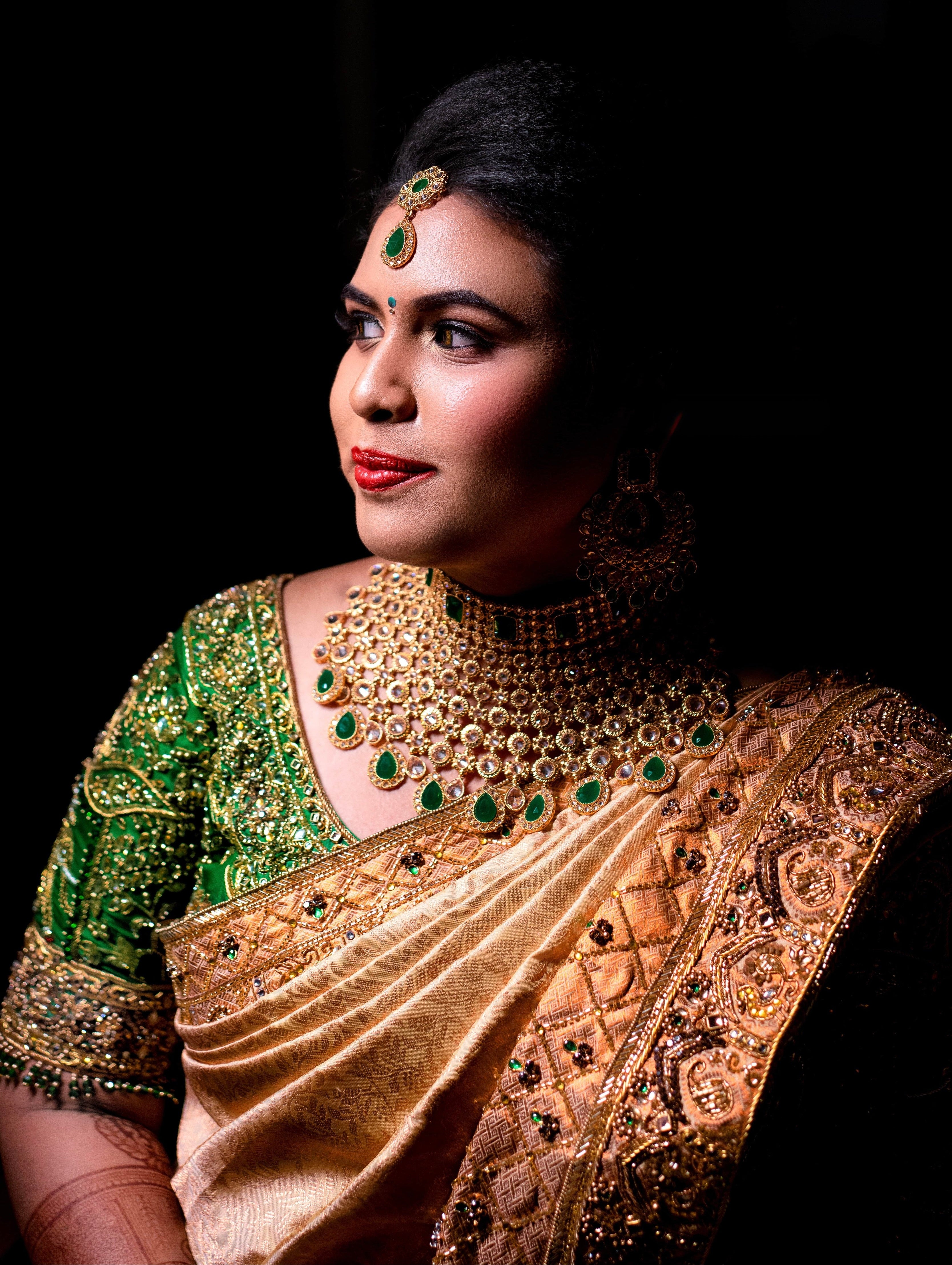 Bride Hemakiruthika from Chennai in a green raw silk blouse and gold silk saree with heavy border embellishments, designed by Archana Karthick. She is looking to her right. it is a closeup shot detailing the saree border and right sleeve.
