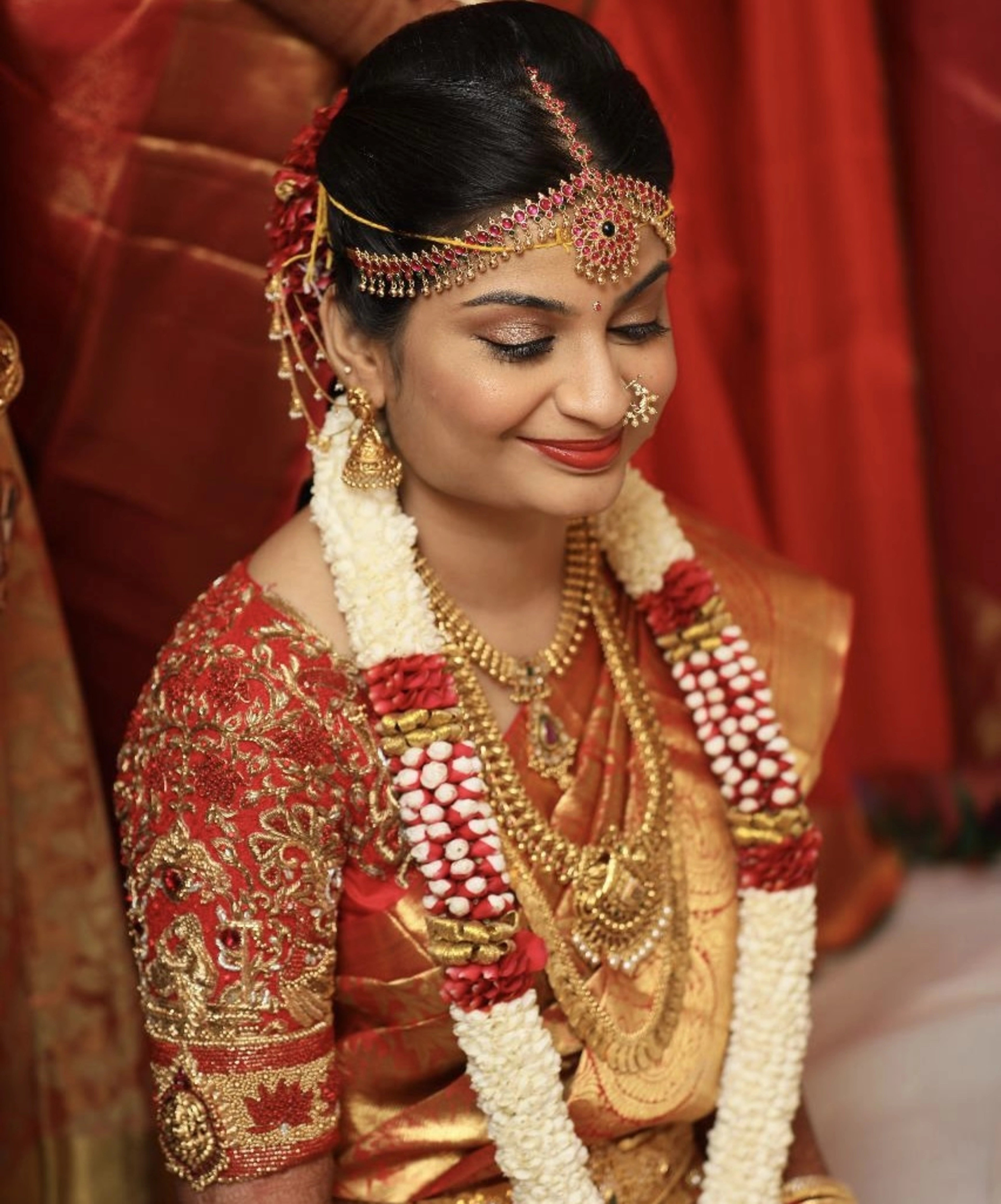 Bride Jashwanti Reddy smiling in a red silk palanquin concept blouse for her wedding, handcrafted with zardozi, resham and beads by team Archana Karthick.