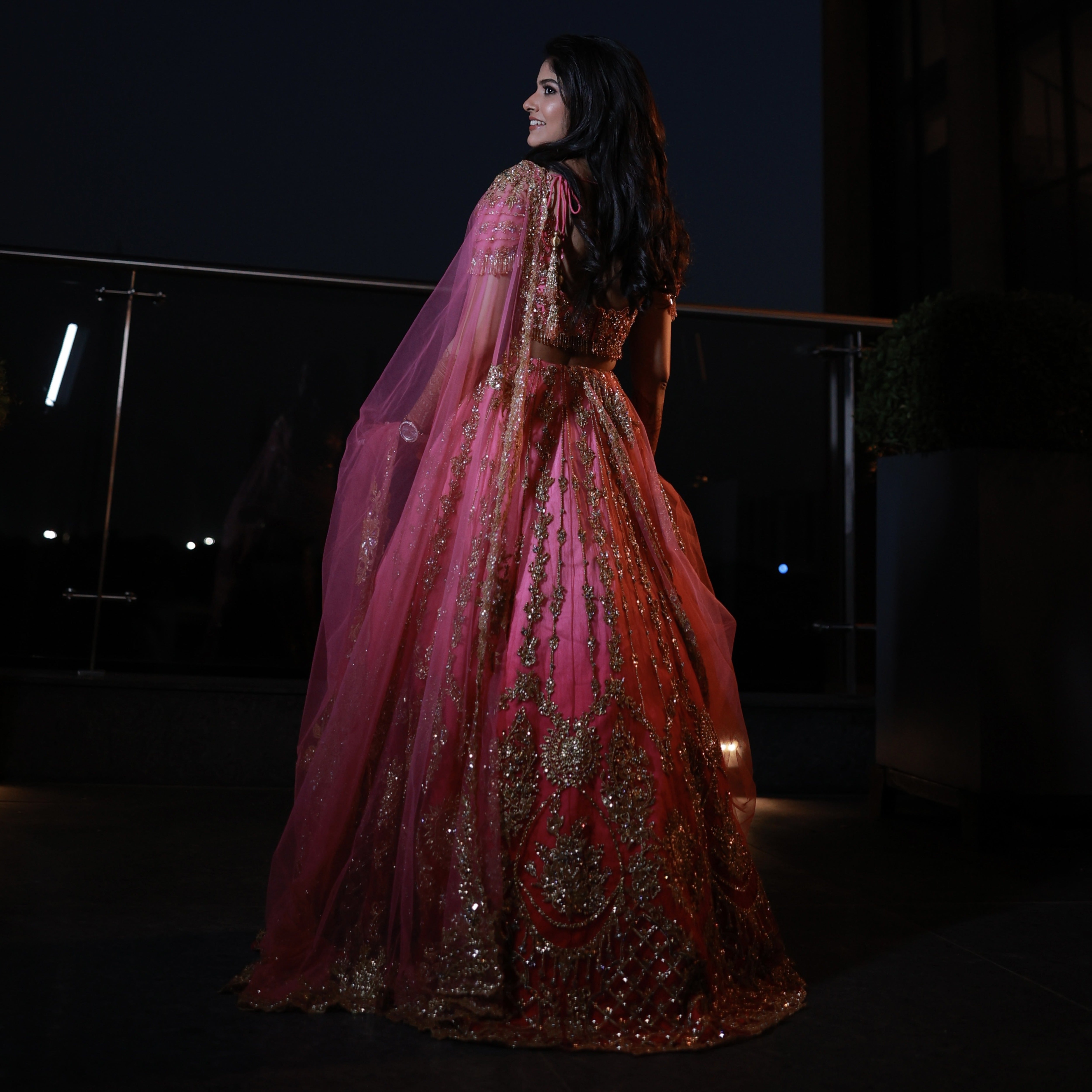 Bride Kaviya from Christchurch, New Zealand posing elegantly in her pink handcrafted reception lehenga with heavy stone work designed by Archana Karthick. Back Lehnega design is captured well.