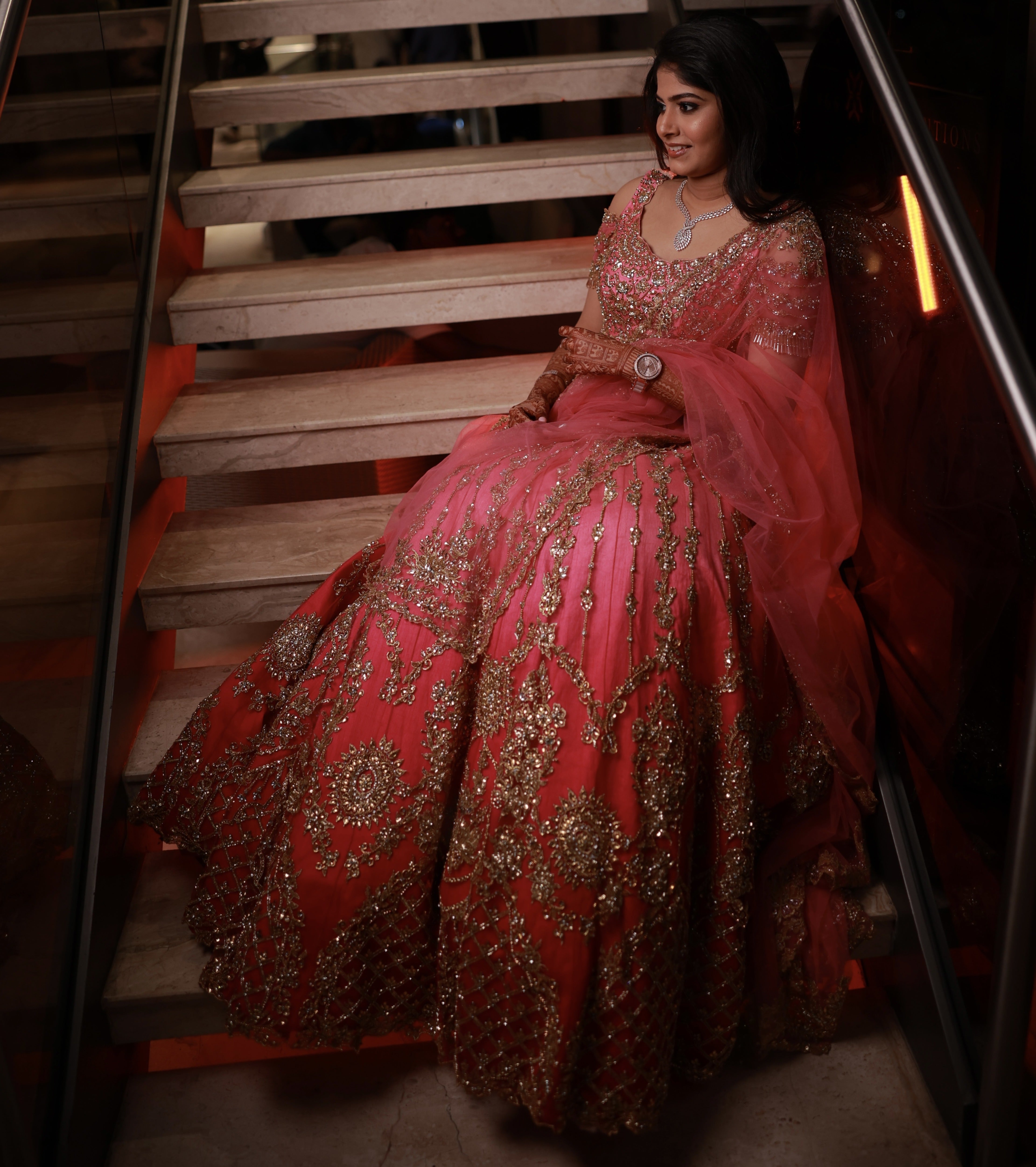 Bride Kaviya from Christchurch, New Zealand seated elegantly on the stairs in her pink handcrafted reception lehenga with heavy stone work designed by Archana Karthick. Front blouse and lehnega design is captured well.