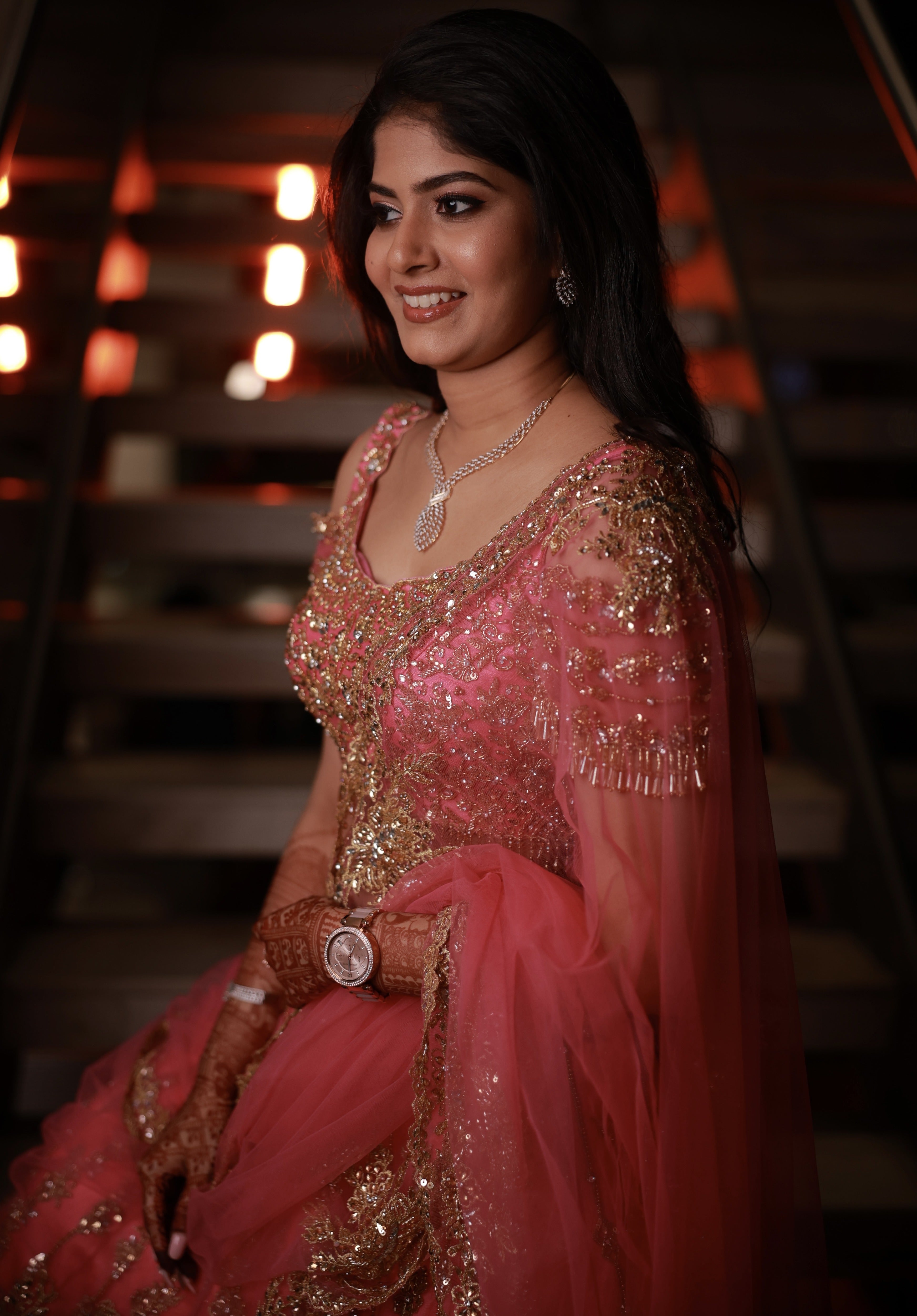 Bride Kaviya from Christchurch, New Zealand standing elegantly on the stairs in her pink handcrafted reception lehenga with heavy stone work designed by Archana Karthick. Front blouse and sleeve design is captured well.