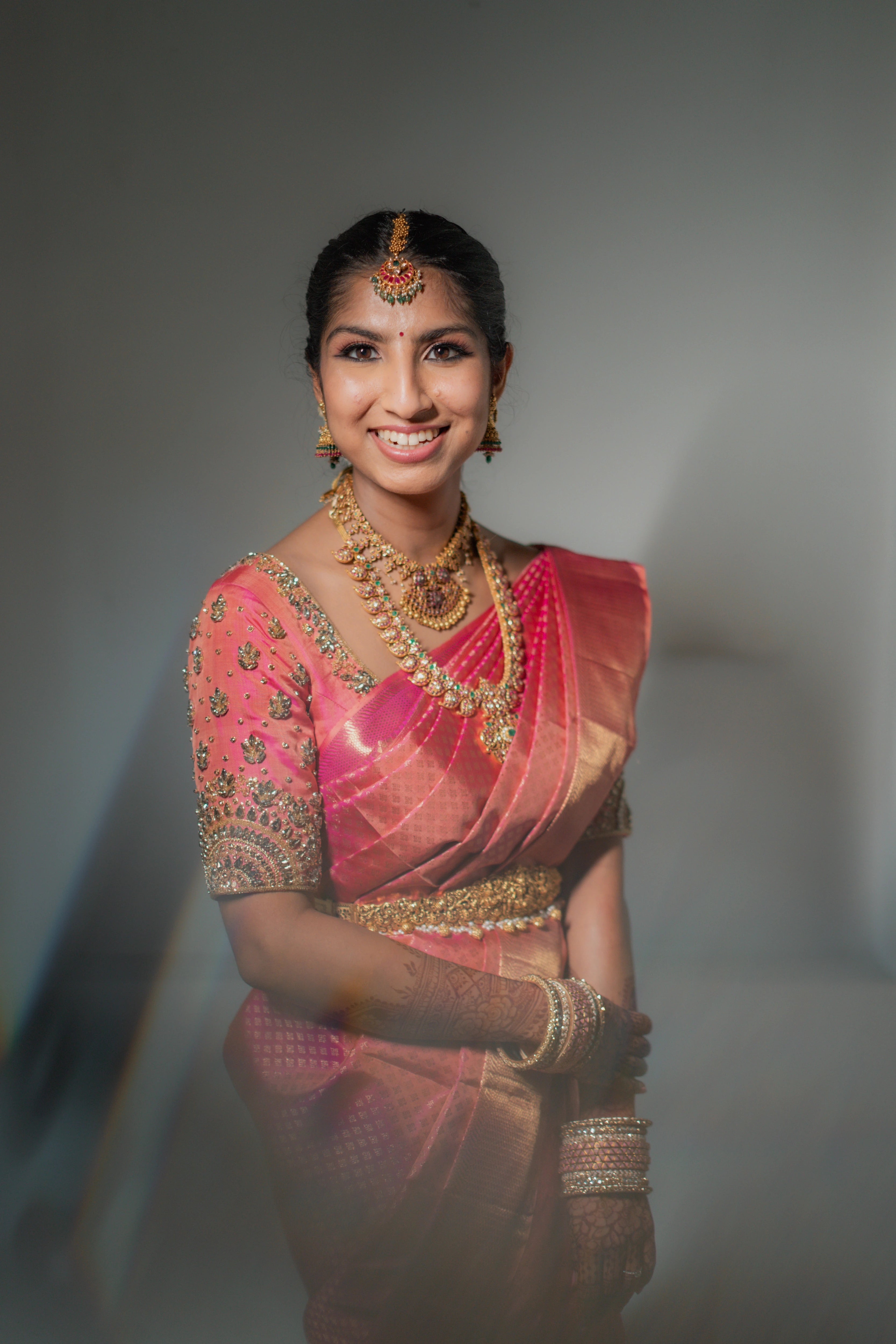 Bride Kavya smiling in a pink raw silk blouse handcrafted by team Archana Karthick.