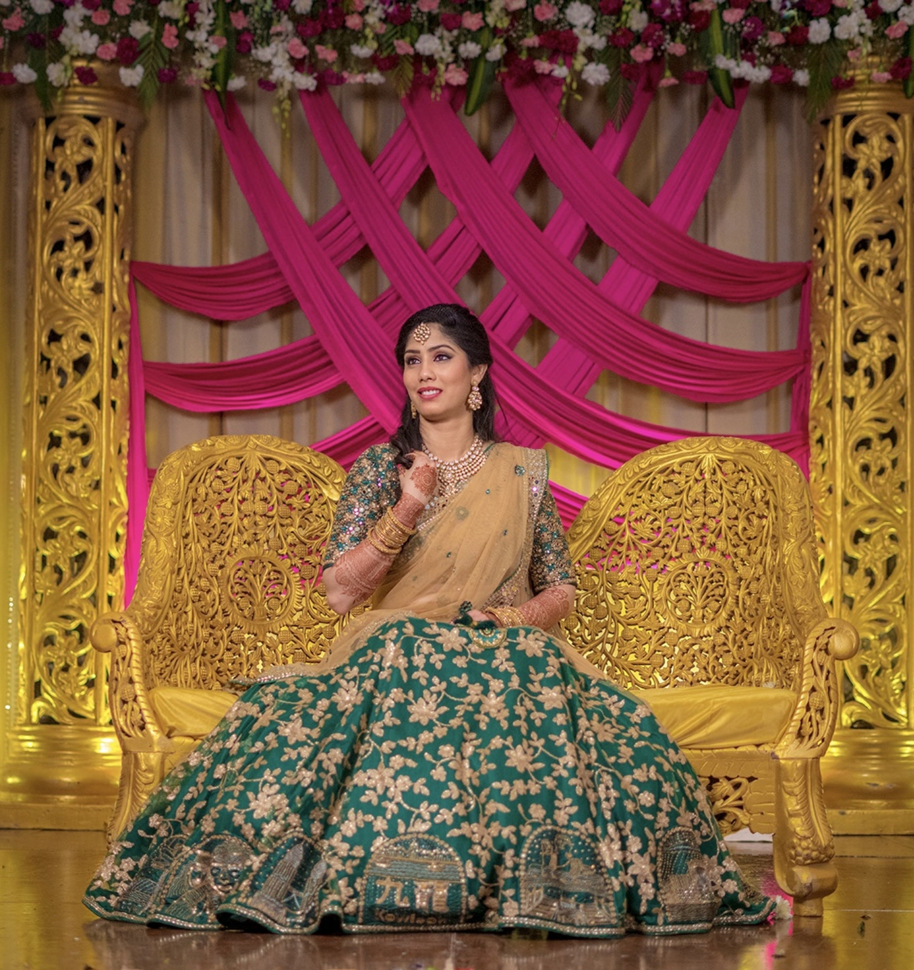 Bride Keerthana, from new zealand in a green handcrafted love story lehenga by Archana Karthick. She is seated on the reception stage couch