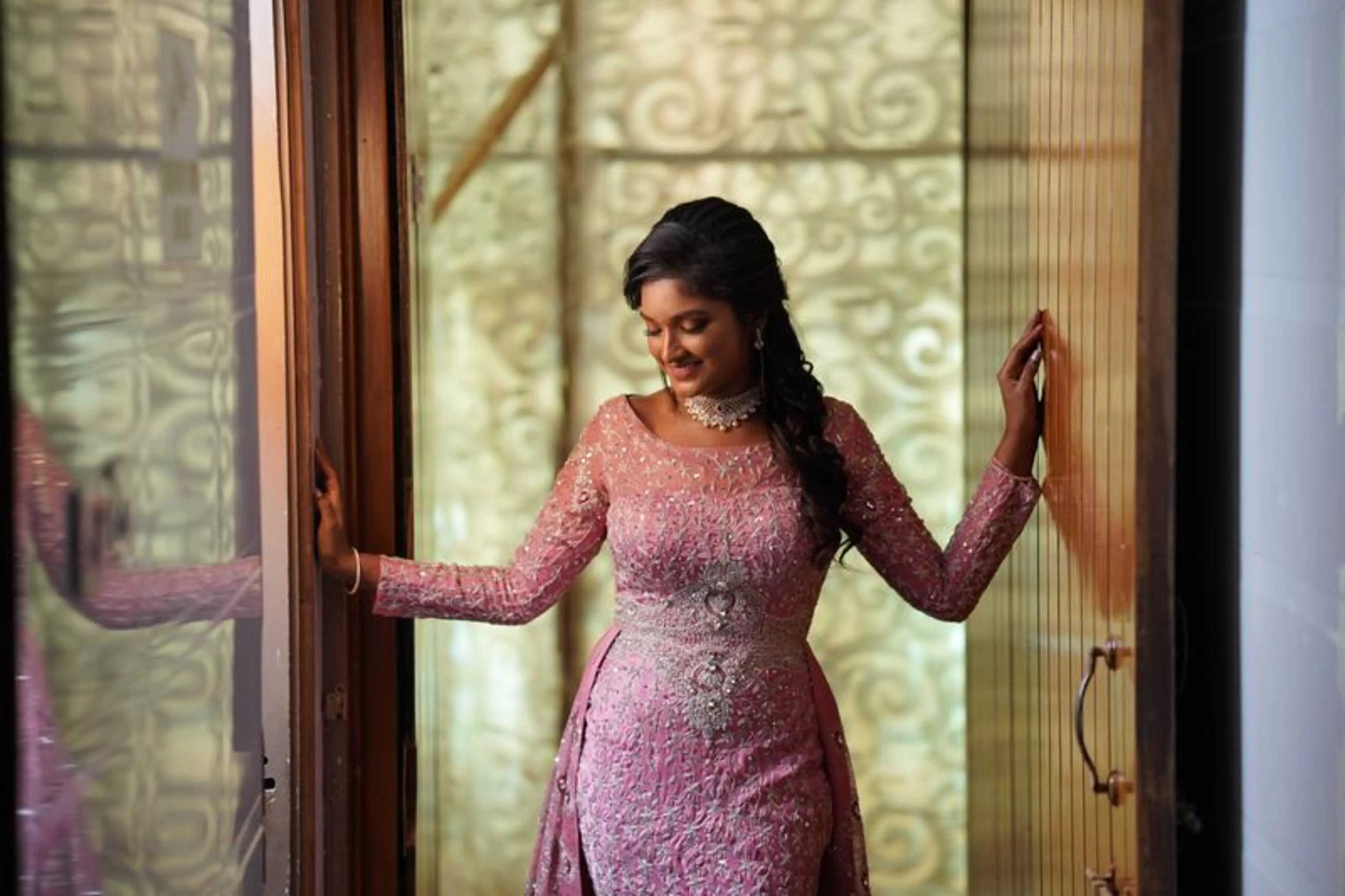 Bride Lavanya posing in a pink satin mermaid gown with attached trail, handcrafted intricately with rhinestones, stones, zardozi and cutdana by team Archana Karthick.
