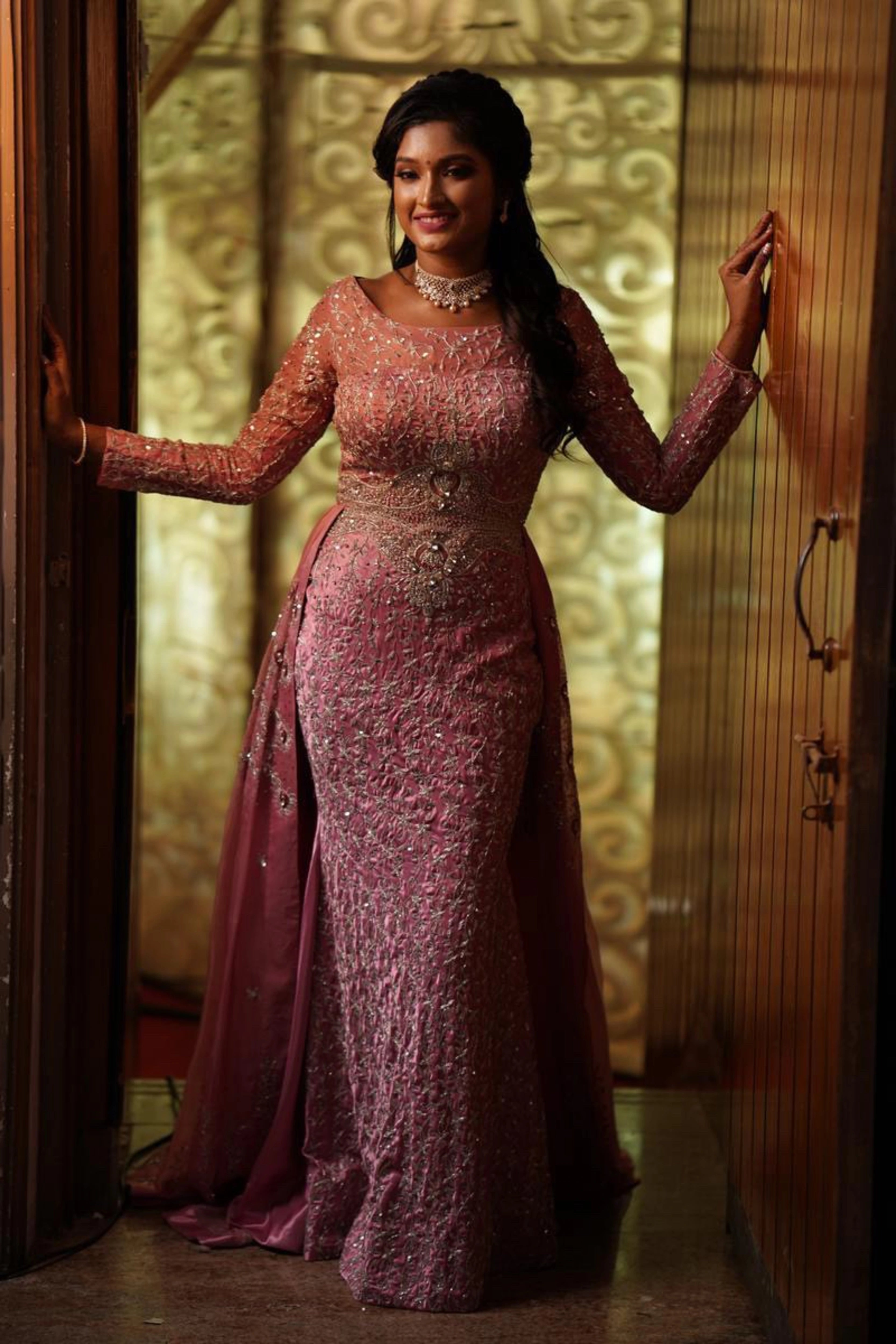 Bride Lavanya smiling in a pink satin mermaid gown with attached trail, handcrafted intricately with rhinestones, stones, zardozi and cutdana by team Archana Karthick.