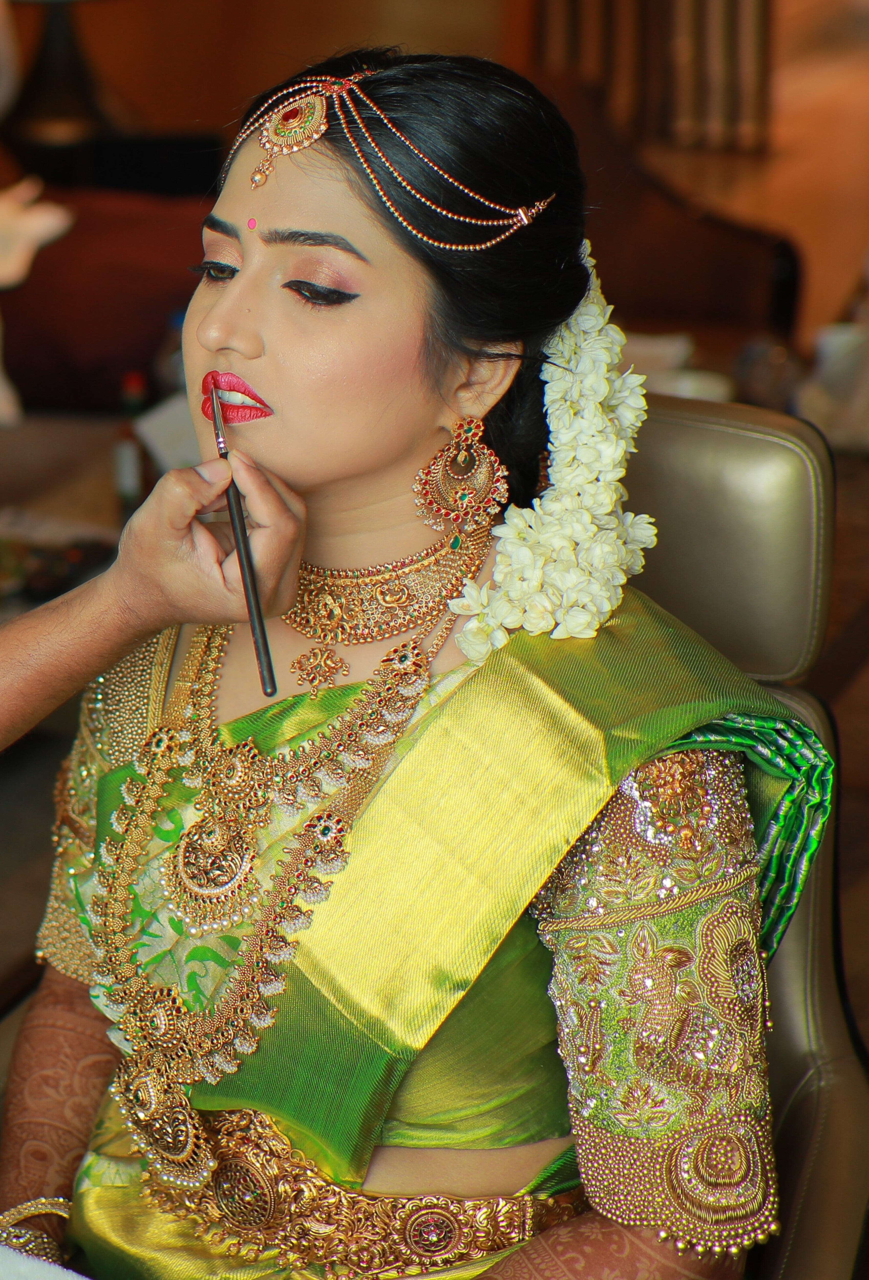 Bride Nivetha during makeup in a lemon green silk blouse, intricately handcrafted with zardozi, beads, stones, nakshi and more by team Archana Karthick.