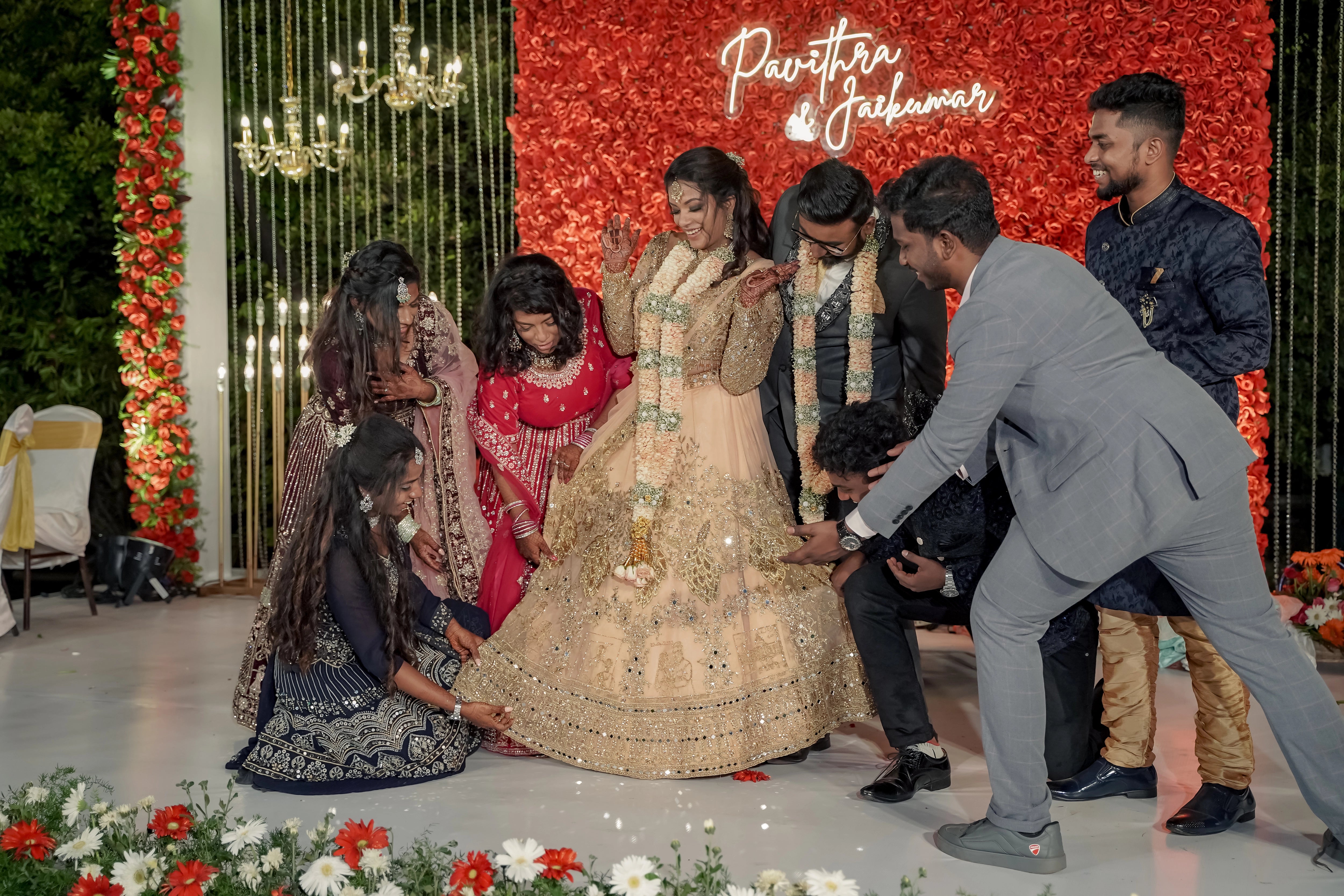 Bride Pavithra & Groom Jai on stage with friends in a beige gold lehenga and charcoal grey suit and intricately handcrafted by team Archana Karthick.