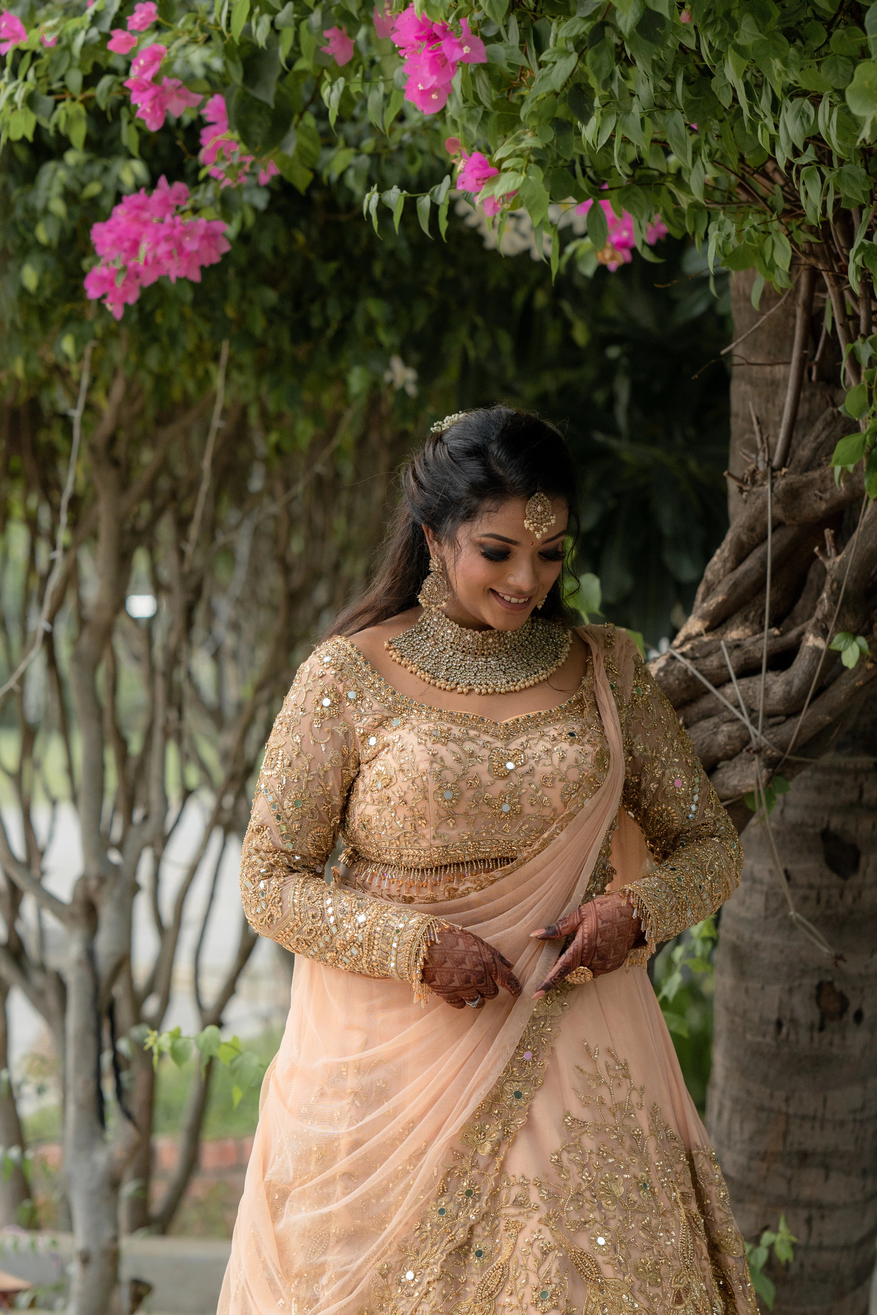 Bride Pavithra smiling in a beige gold tulle lehenga, intricately handcrafted with mirrors, sequins, cutdana, beads, crystals and resham by team Archana Karthick.