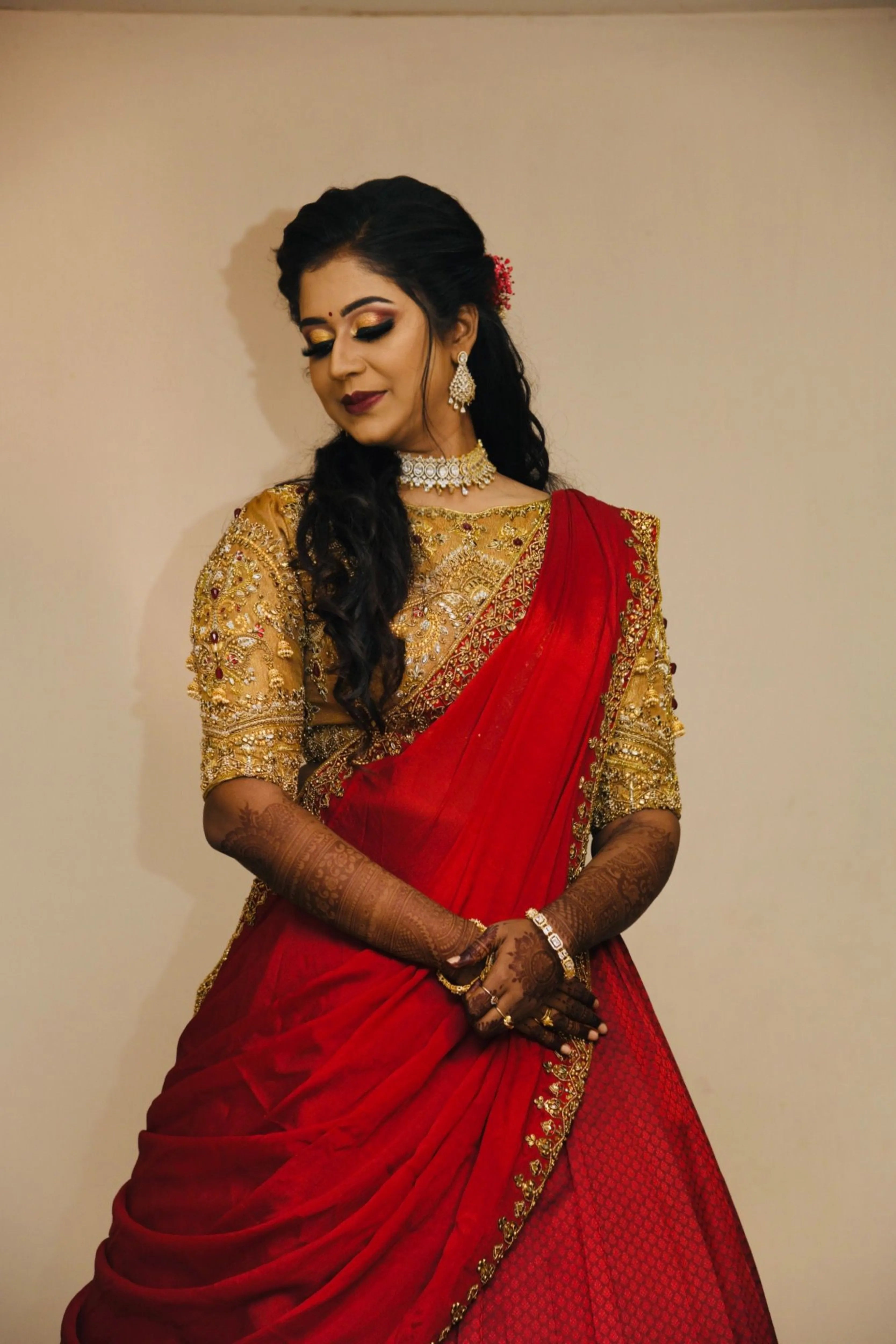 Bride Raji from Ireland smiling in a red and gold silk half saree during makeup, handcrafted intricately with stones, zardozi, beads, sequins and rhinestones by team Archana Karthick