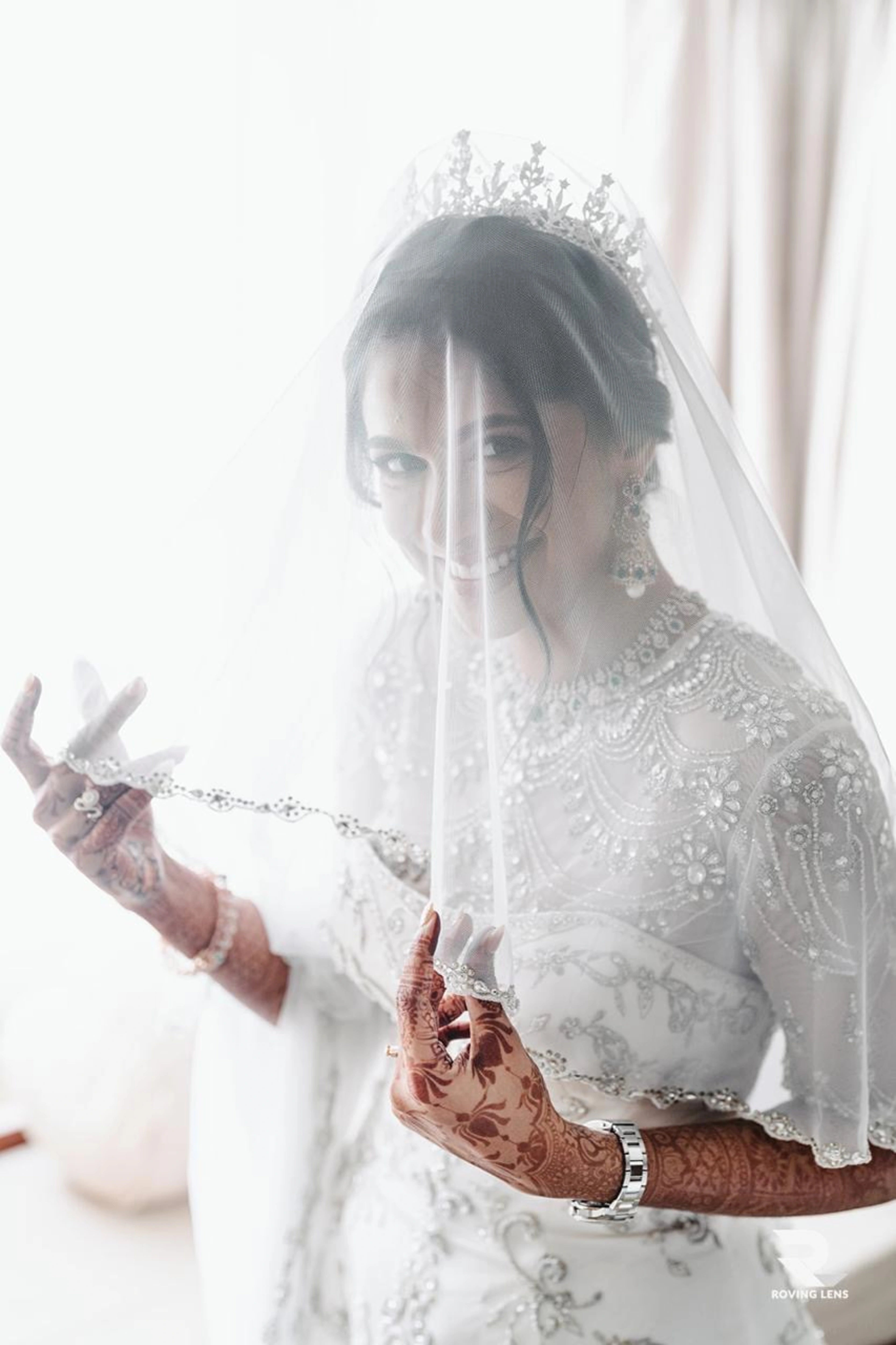 Bride Roushni smiling under the veil in a white gown for her church wedding by team Archana Karthick.