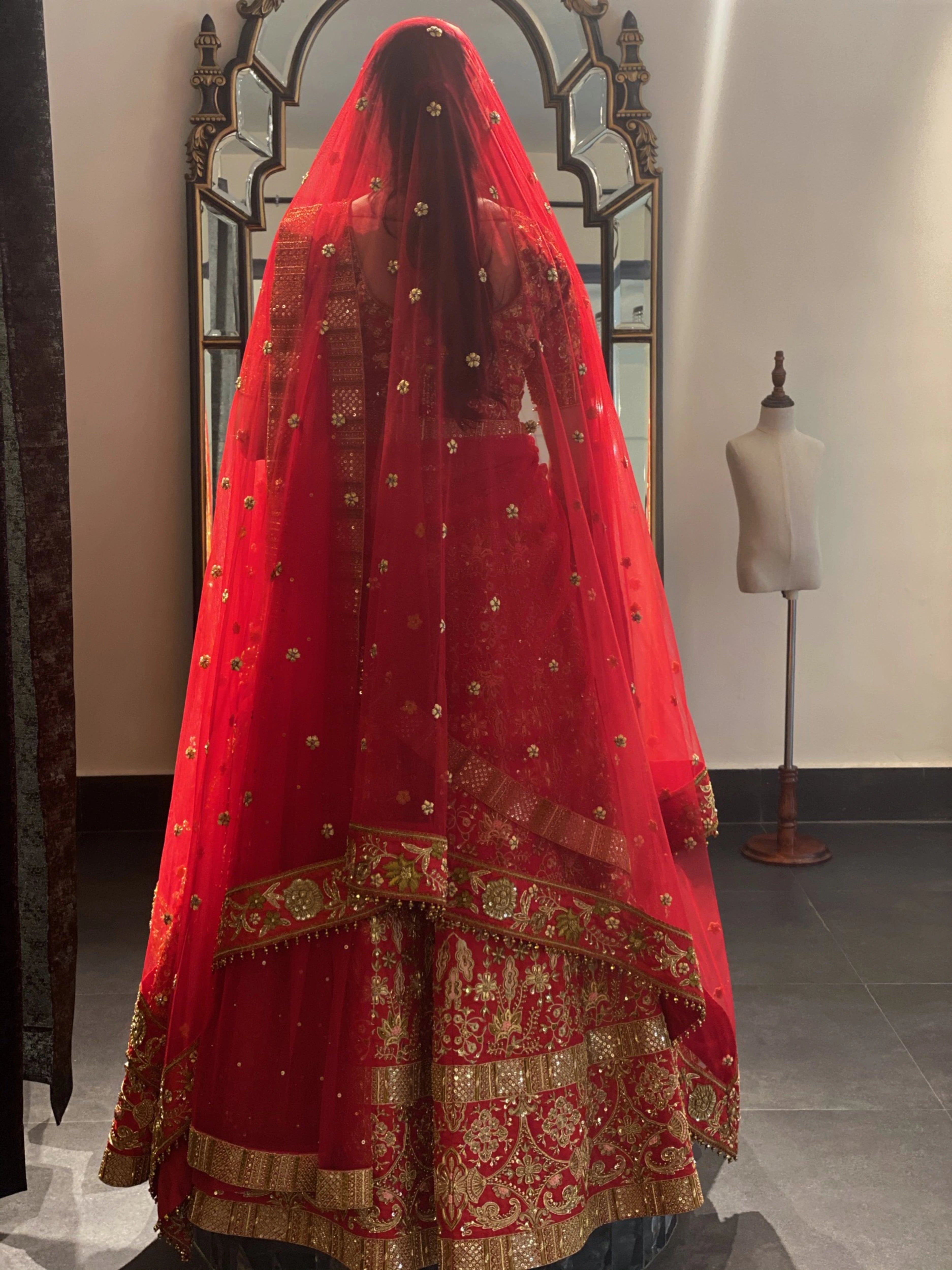 Bride Saba during fittings in a red raw silk lehenga with a veil and dupatta handcrafted by team Archana Karthick.