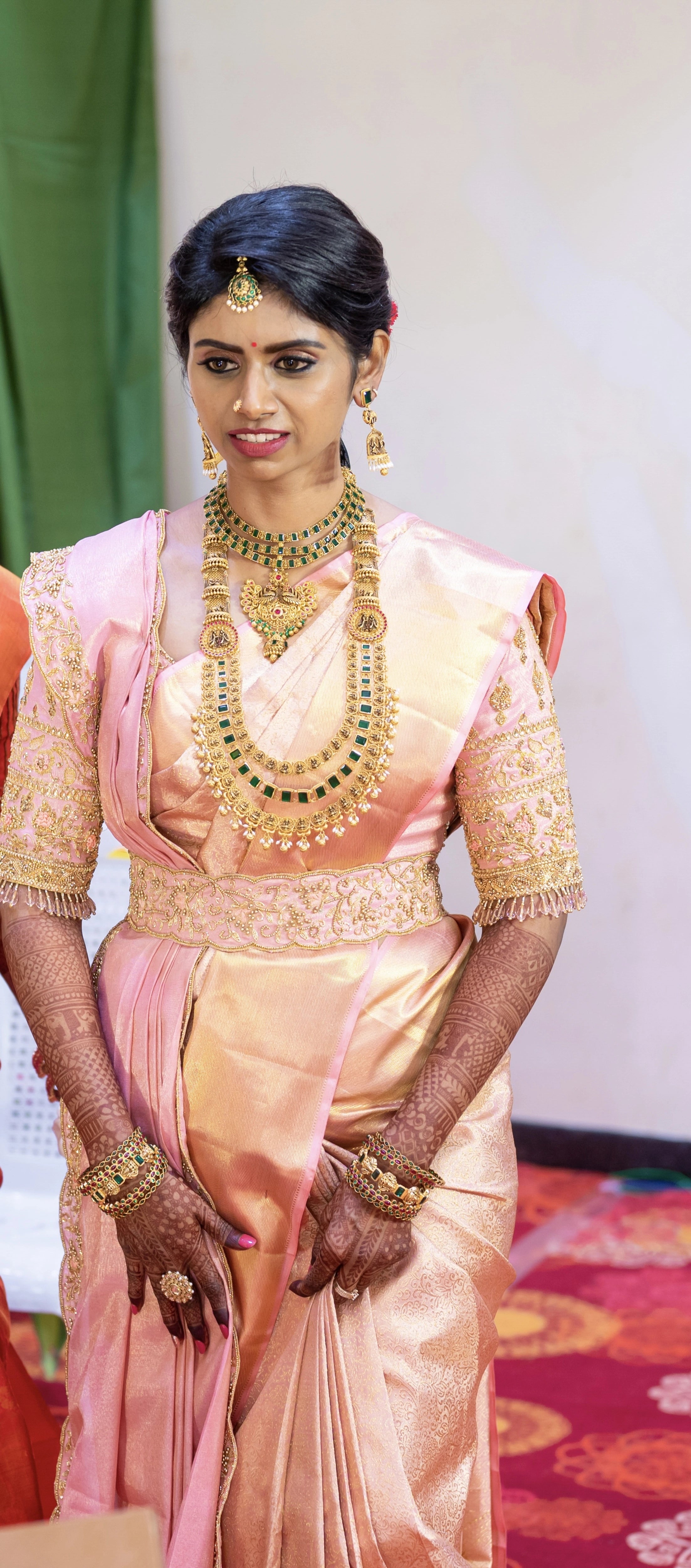 Bride Sahana posing on stage in a peach cream silk blouse and belt, handcrafted intricately with beads, cutdana, zari, crystals and resham by team Archana Karthick.