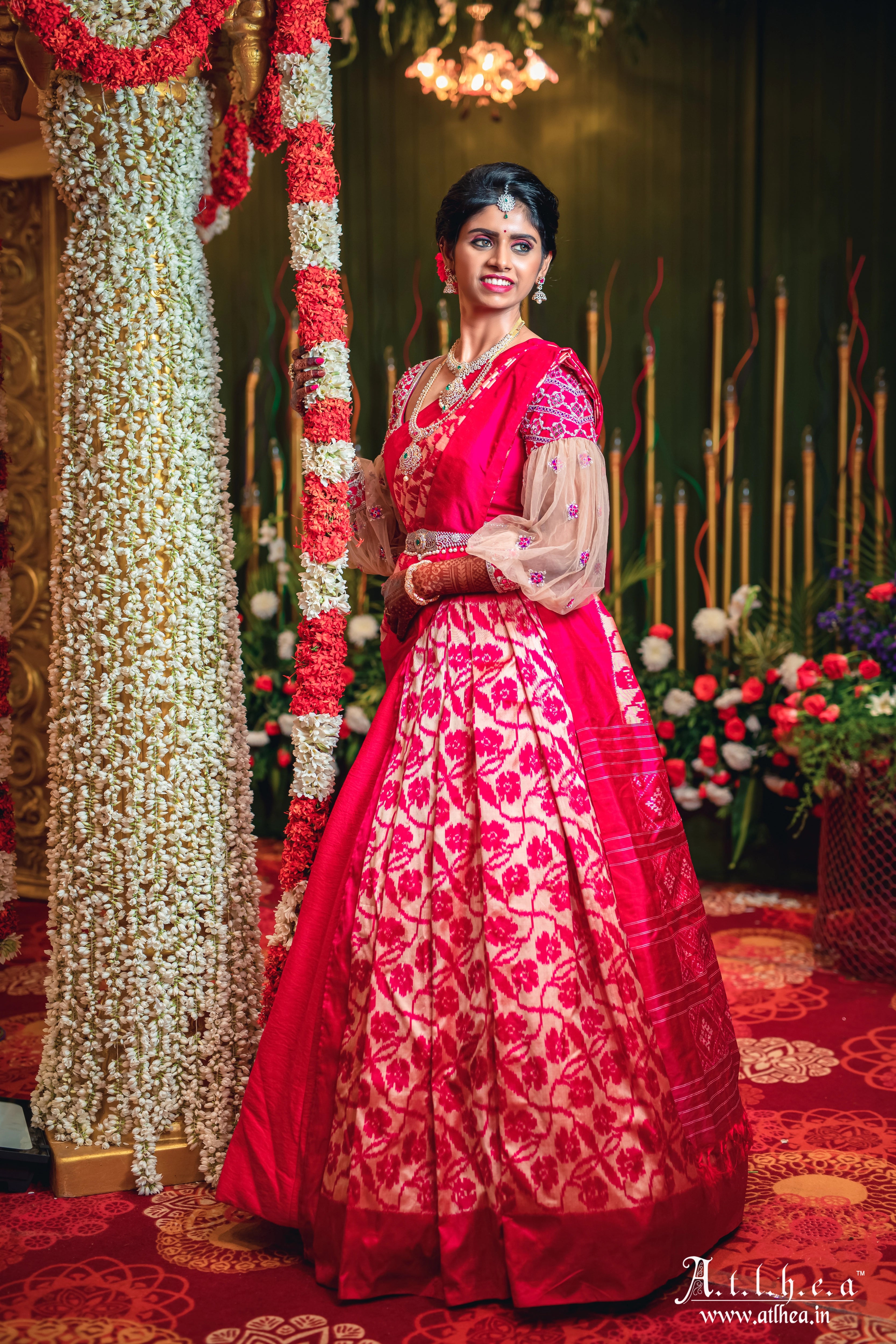 Bride Sahana posing with smile in a raspberry raw silk half saree, handcrafted intricately with mirror, stones, zardozi and resham by team Archana Karthick.