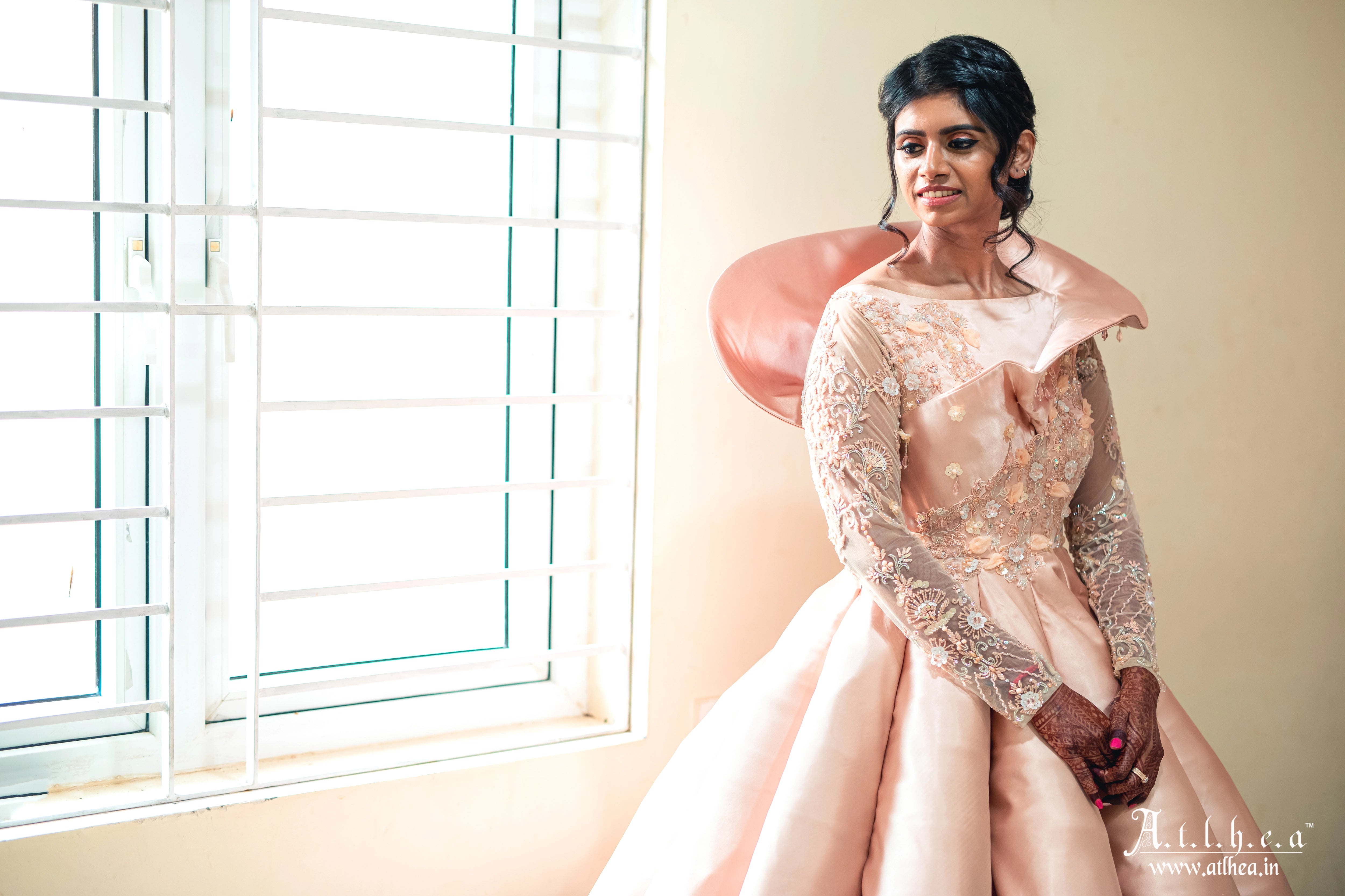 Bride Sahana smiling in a peach cream satin structured ball gown, handcrafted intricately with applique, sequins, stones and cutdana by team Archana Karthick.