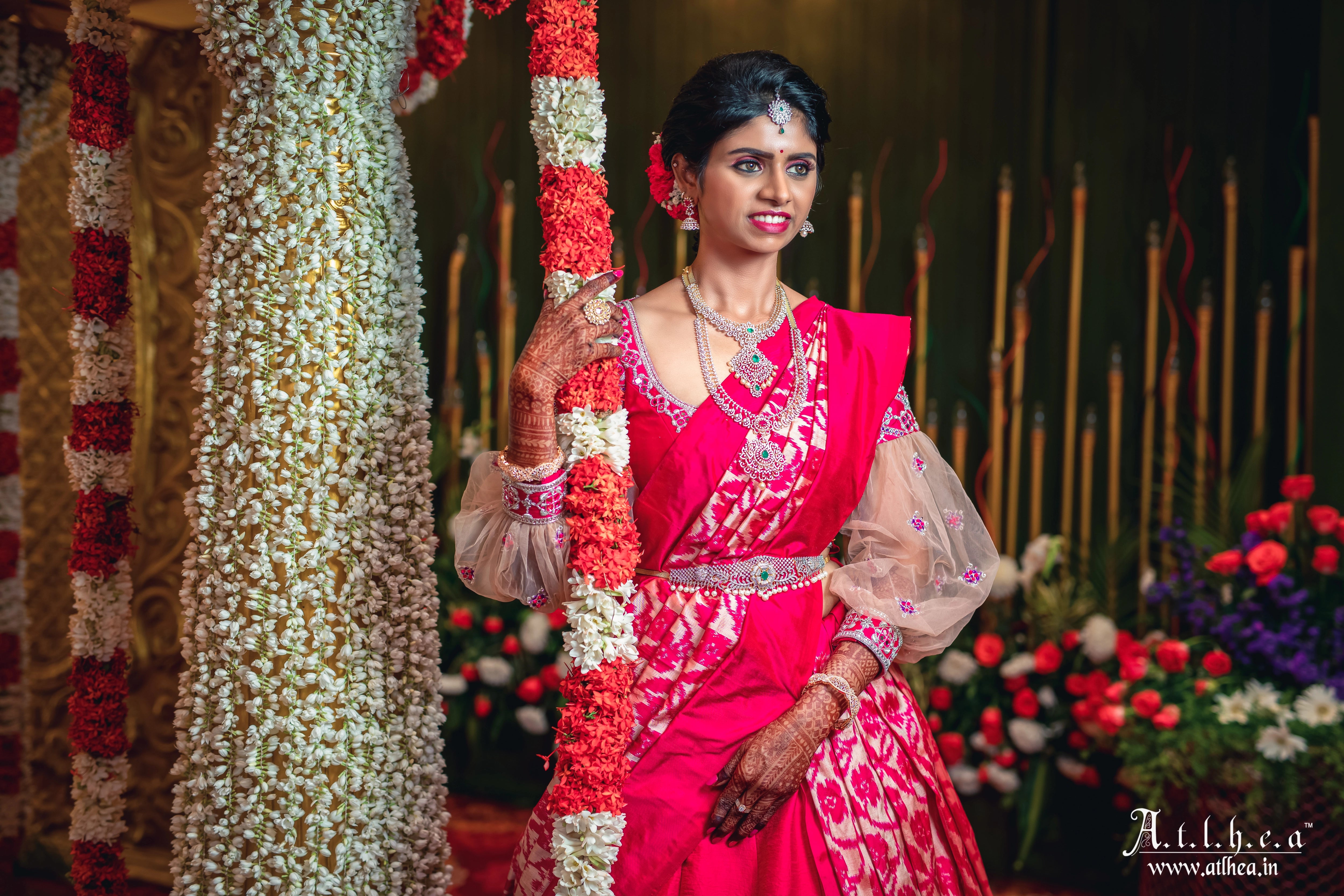 Bride Sahana smiling in a raspberry raw silk half saree, handcrafted intricately with mirror, stones, zardozi and resham by team Archana Karthick.