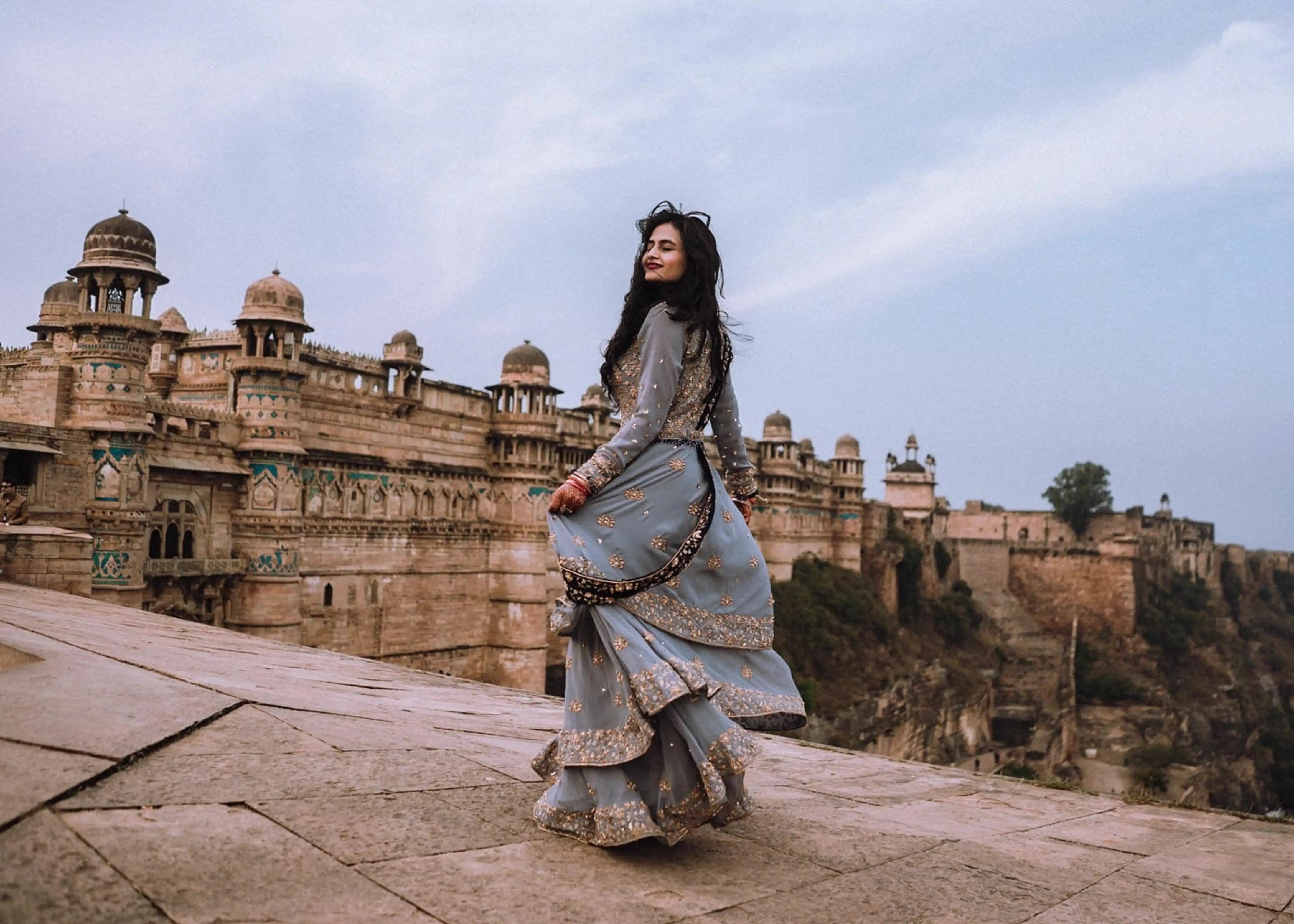 Bride Sapna Tapadia from Australia posing in a layered gown in aqua grey georgette, paired with a navy blue dupatta. Intricately handcrafted by team Archana Karthick.