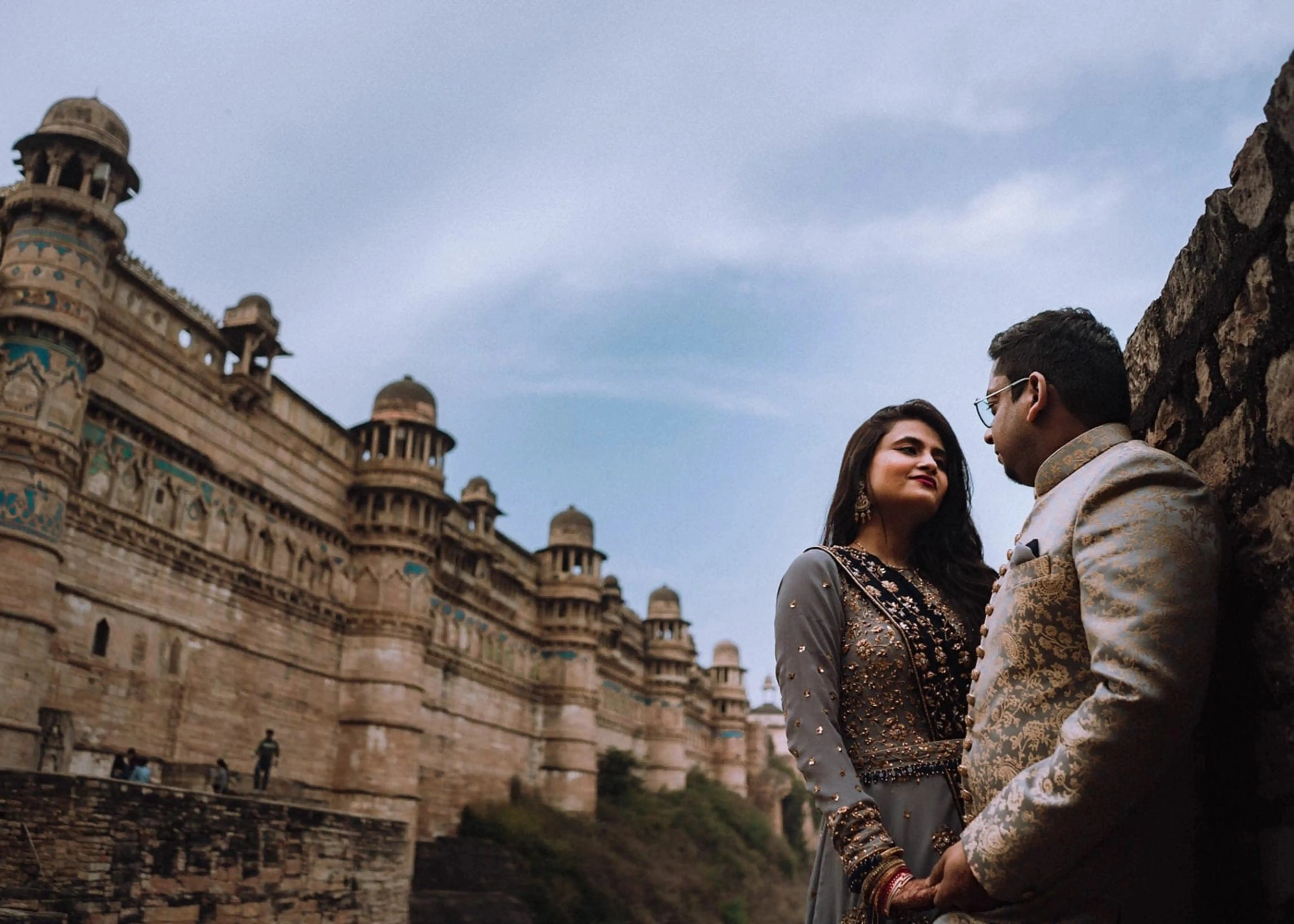 Bride Sapna Tapadia from Australia posing with groom in a layered gown in aqua grey georgette, paired with a navy blue dupatta. Intricately handcrafted by team Archana Karthick.