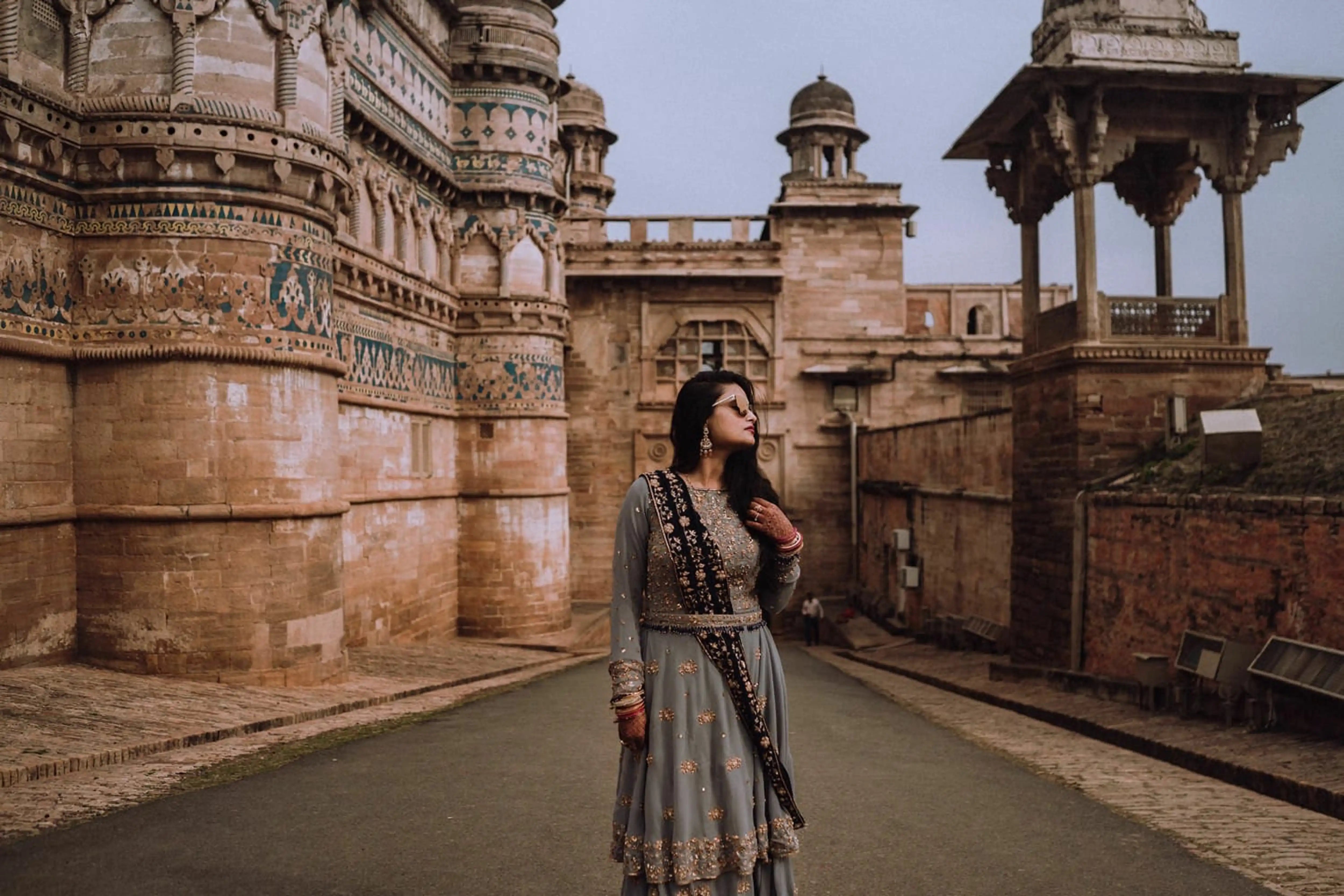 Bride Sapna Tapadia from Australia posing with sunglasses in a layered gown in aqua grey georgette, paired with a navy blue dupatta. Intricately handcrafted by team Archana Karthick.