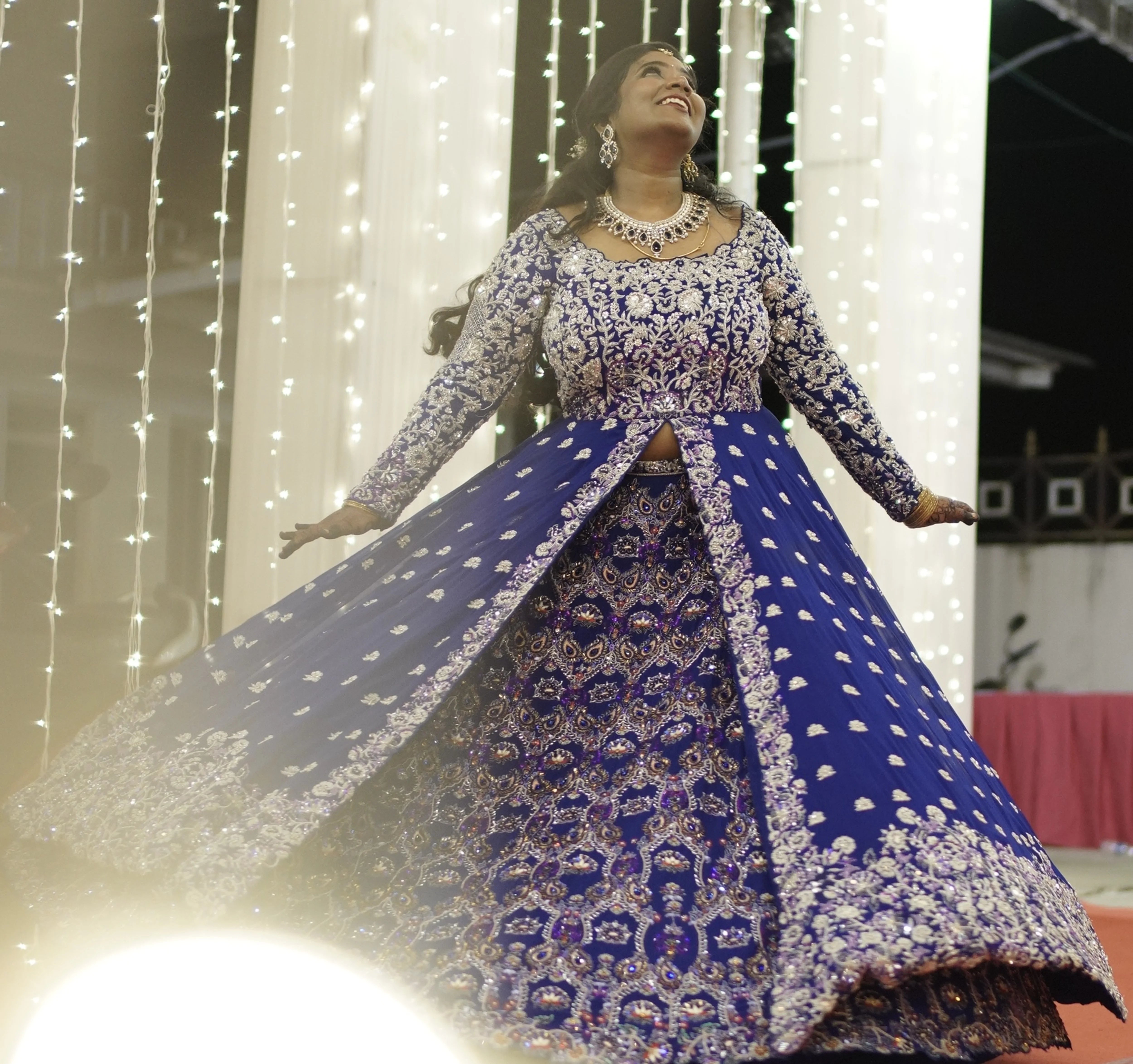 Bride Sathiyapriya twirling and looking up in a midnight blue georgette masakali lehenga for her reception in Dindigul