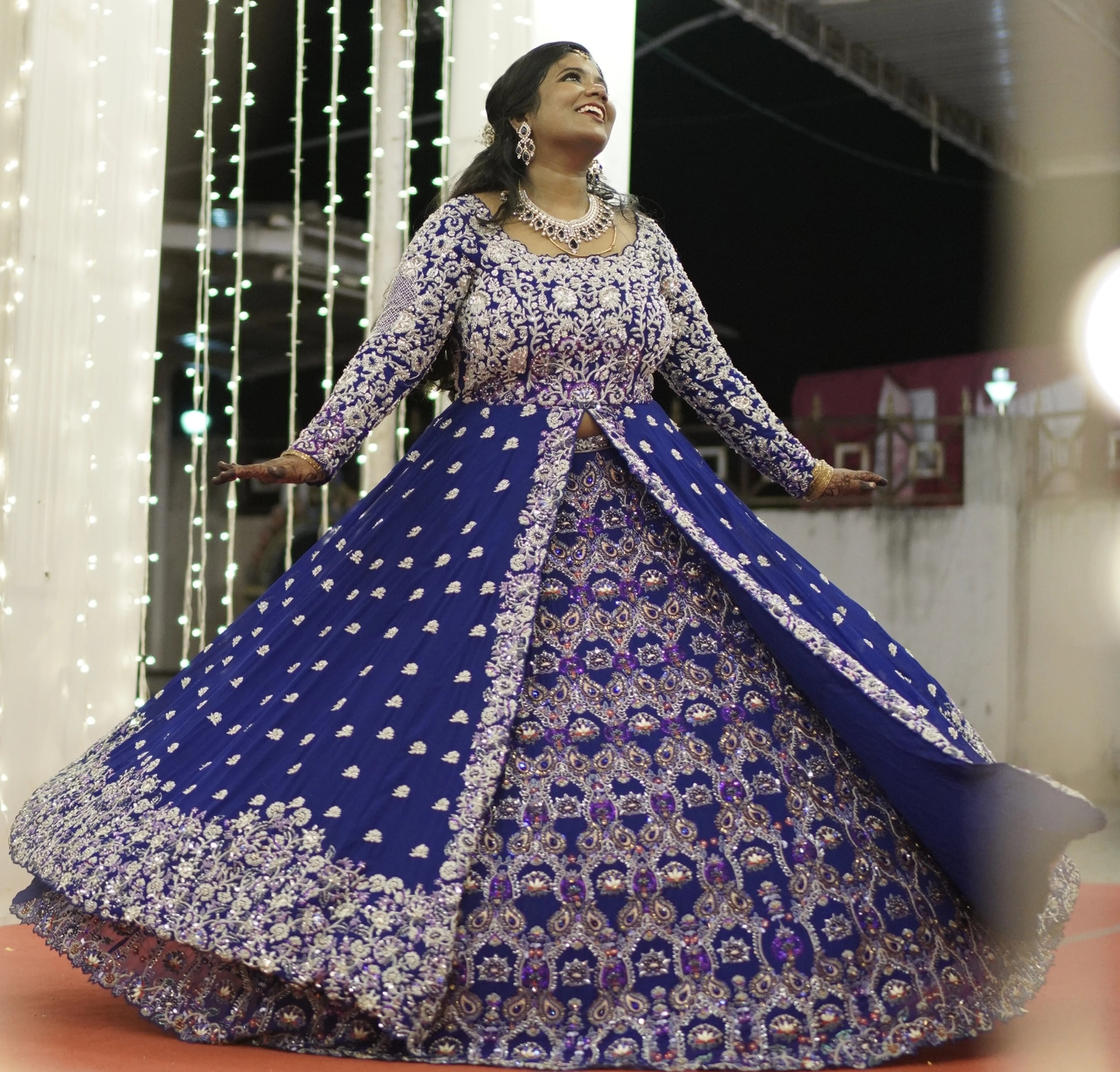 Bride Sathiyapriya twirling and looking up to her left in a midnight blue georgette masakali lehenga for her reception in Dindigul