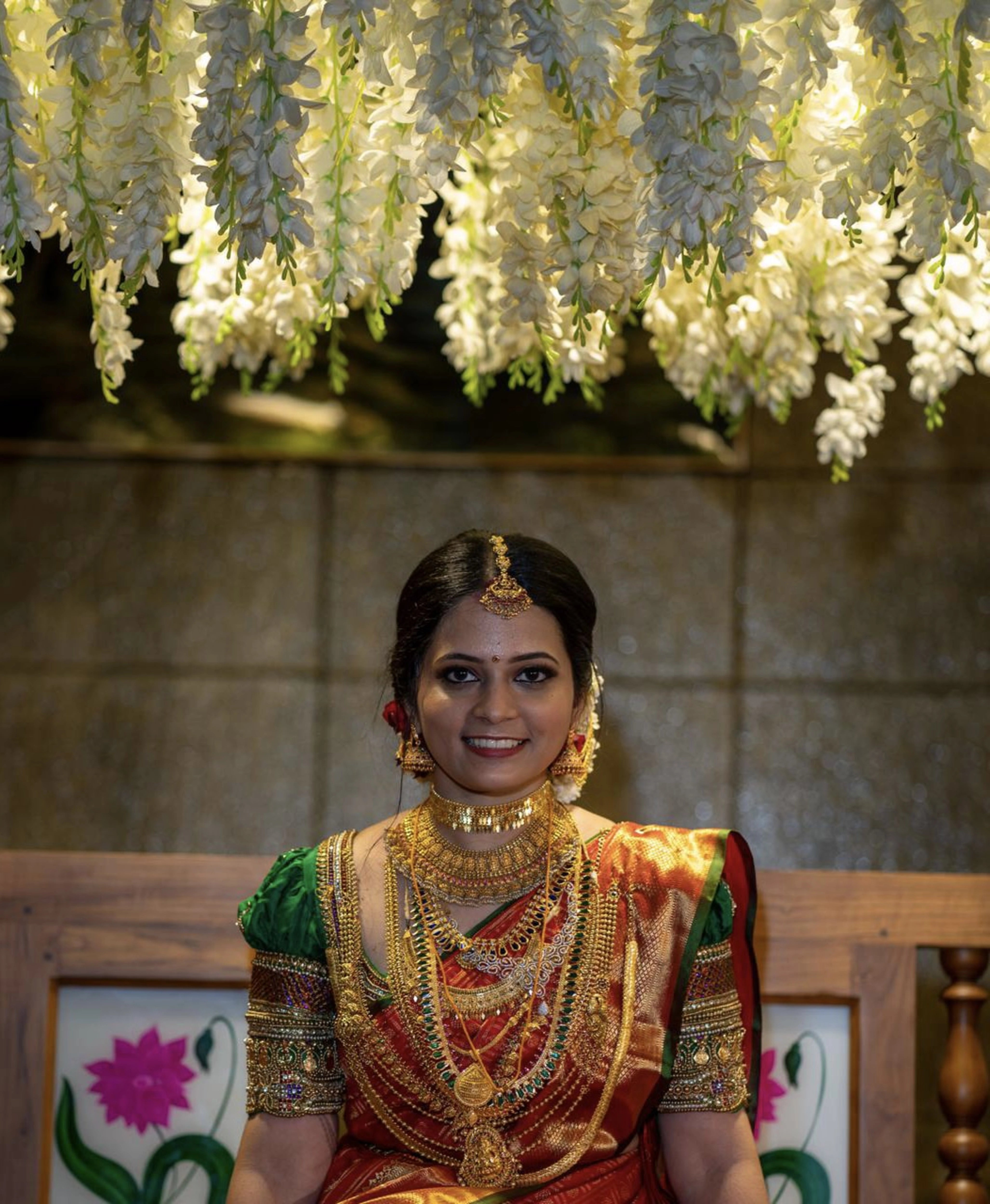 Bride Shalini from Kerala under floral decor in a handcrafted green silk blouse embellished with beads, zardozi, kundan, kemp stones, coins & pearls by team Archana Karthick.