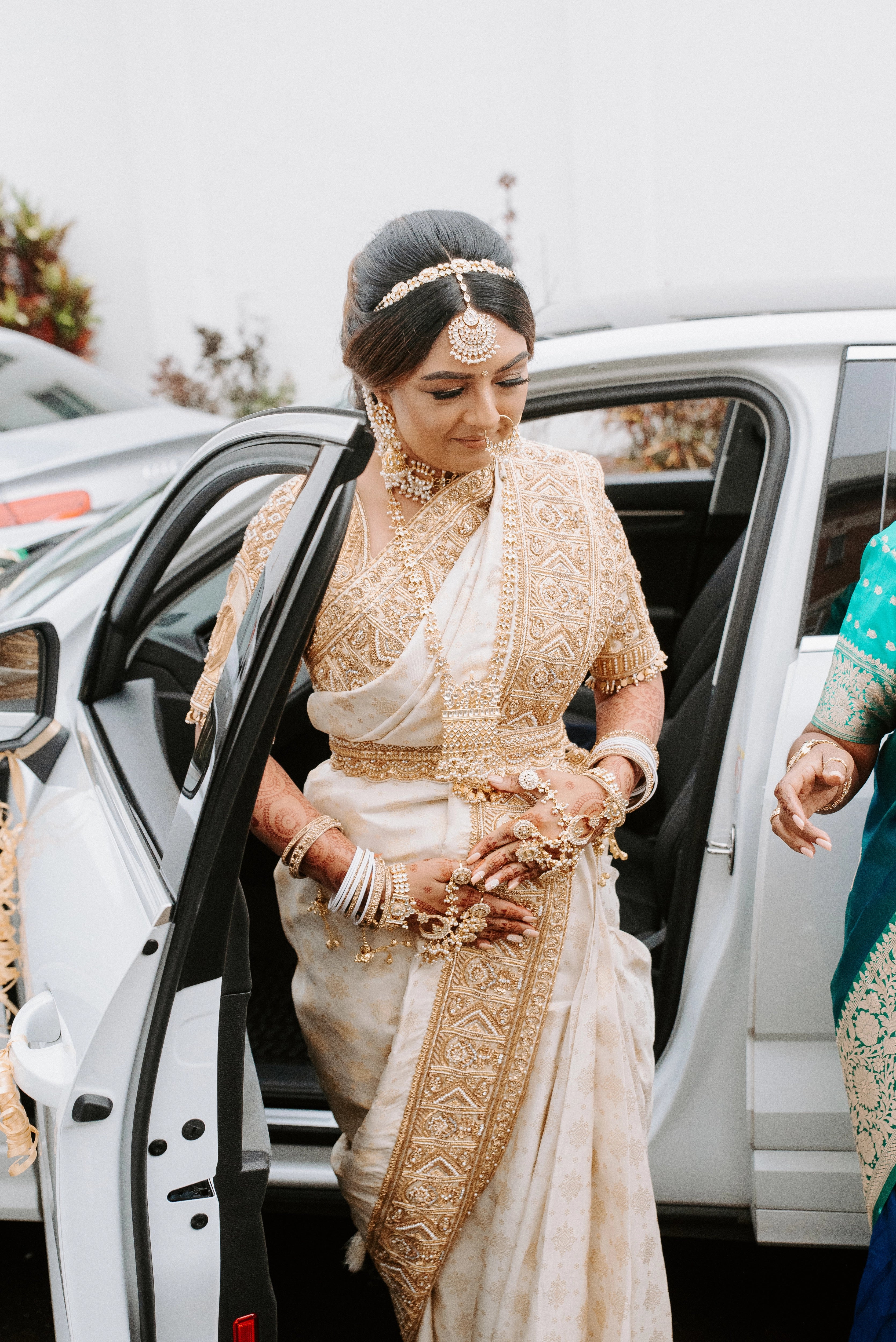 Bride Shayal Raniga getting out of a car in an ivory silk concept blouse & saree border, intricately handcrafted with zardozi, stones, pearls and coins by team Archana Karthick.